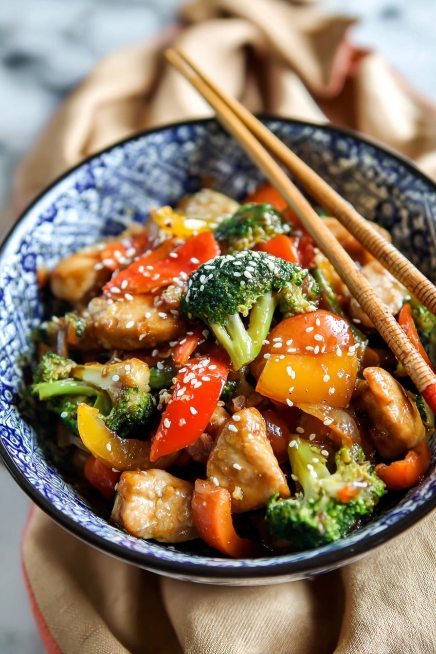 A bowl with blue and white patterned design holds a colorful stir-fry dish. The bottom layer is juicy, light brown pieces of chicken. Mixed with the chicken are bright green broccoli florets, orange carrot slices, and chunks of red and yellow bell peppers. The vegetables appear fresh and slightly glossy with sauce. White sesame seeds sprinkled on top add texture. Two wooden chopsticks stand upright in the bowl. The bowl sits on a tan fabric on a white marbled surface. Photo taken with an iphone --ar 2:3 --v 7 - Easy Chicken Stir Fry with Veggies, chicken stir fry recipes, quick healthy chicken dishes, flavorful stir fry dinner ideas, easy weeknight chicken recipes