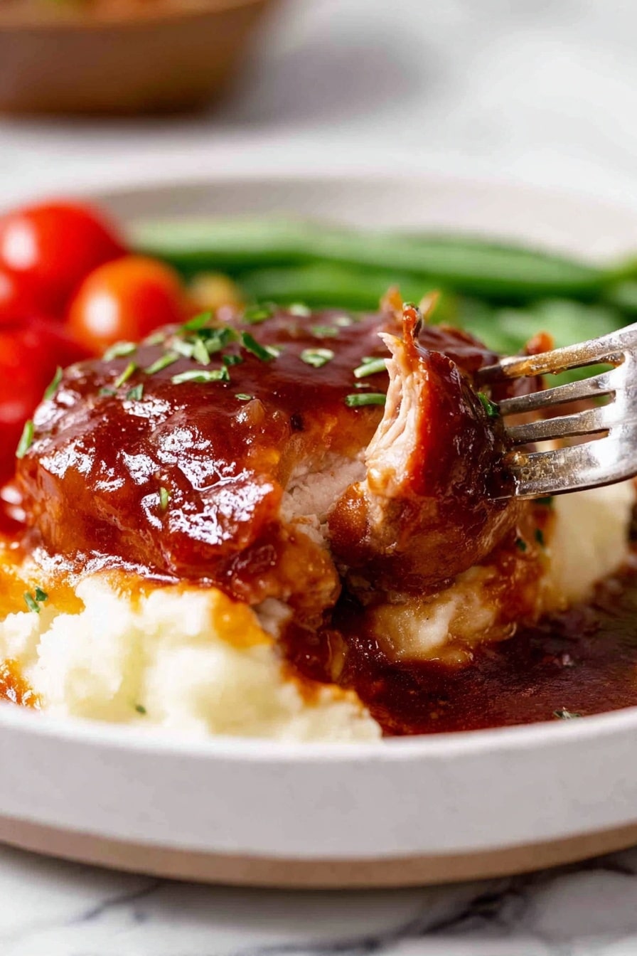 A white plate filled with three layers: the bottom layer is creamy mashed potatoes with a smooth texture, the middle layer is a thick piece of cooked meat topped with a shiny reddish-brown sauce, and the top layer has small green herb pieces sprinkled over the sauce. On the side of the plate, there are blurred cherry tomatoes and green beans adding red and green colors in the background. A fork is holding a piece of the meat, lifting it slightly from the plate. The dish is set on a white marbled surface. Photo taken with an iphone --ar 2:3 --v 7 - Oven Baked BBQ Chicken, Homemade BBQ Sauce, Easy BBQ Chicken Recipe, Juicy baked chicken, Smoked flavor oven baked chicken