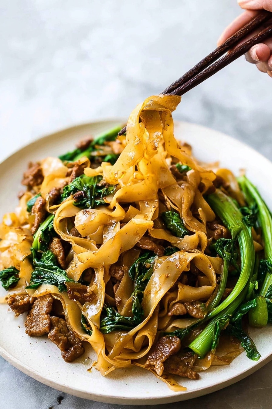 This image shows a white plate filled with wide flat light brown noodles mixed with small pieces of browned meat and bright green leafy vegetables. The noodles look soft and slightly oily, hanging in strands from dark brown chopsticks held by a woman's hand. The meat pieces are scattered throughout the dish, with some near the edges and some under the noodles. The green vegetables add a fresh look, with stems and leaves placed mostly on the right side of the plate. The background is a soft white marbled texture, keeping the focus on the colorful noodles and greens. Photo taken with an iphone --ar 2:3 --v 7 - Authentic Thai Pad See Ew with Chicken, Thai noodle stir-fry recipe, easy Thai chicken stir-fry, homemade Pad See Ew, Thai street food at home