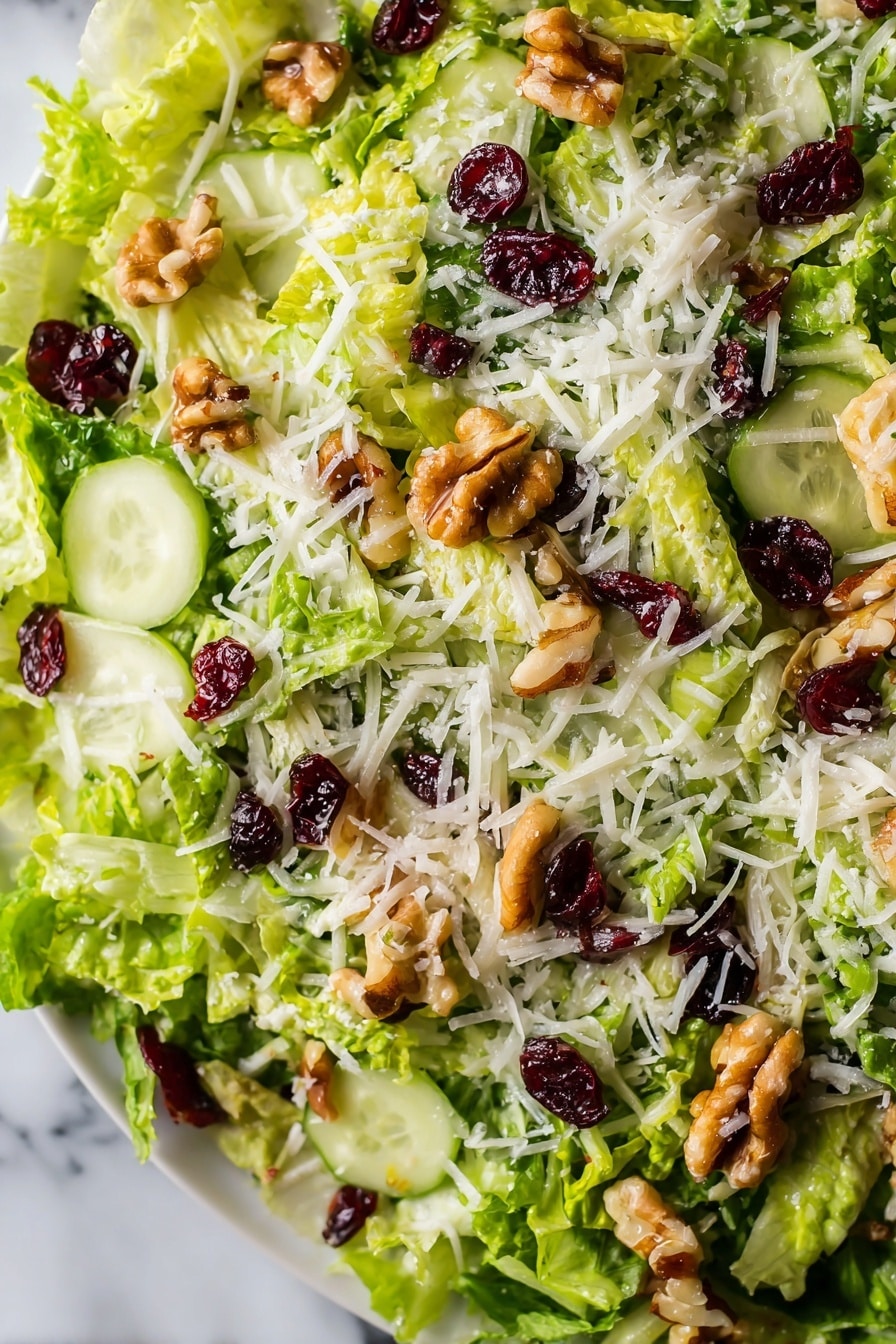 The image shows a close-up view of a fresh salad with several layers. The base layer consists of thinly shredded bright green lettuce. Scattered on top are thin slices of pale green cucumber, adding a smooth texture. There are pieces of light brown walnuts sprinkled across, giving a rough, chunky look. Interspersed are small dark red dried cranberries providing contrasting color and texture. The final layer is a light dusting of white shredded cheese spread evenly over the top. The salad is on a white plate placed over a white marbled surface. photo taken with an iphone --ar 2:3 --v 7 - Crispy Brussels Sprouts Salad with Apples, healthy Brussels sprouts salad, easy autumn salad, crunchy Brussels sprouts apple salad, flavorful vegetarian salad