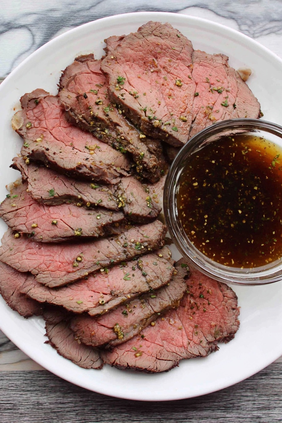 A white plate filled with several thin slices of roast beef, showing pink centers and darker brown edges with visible seasoning and small green herb bits. On the side of the plate, there is a clear glass bowl filled with a dark brown, speckled dipping sauce. The plate is placed on a white marbled surface. photo taken with an iphone --ar 2:3 --v 7 - Beef Top Round Roast, top round beef roast recipe, tender beef roast, easy beef roast, budget-friendly beef dinner