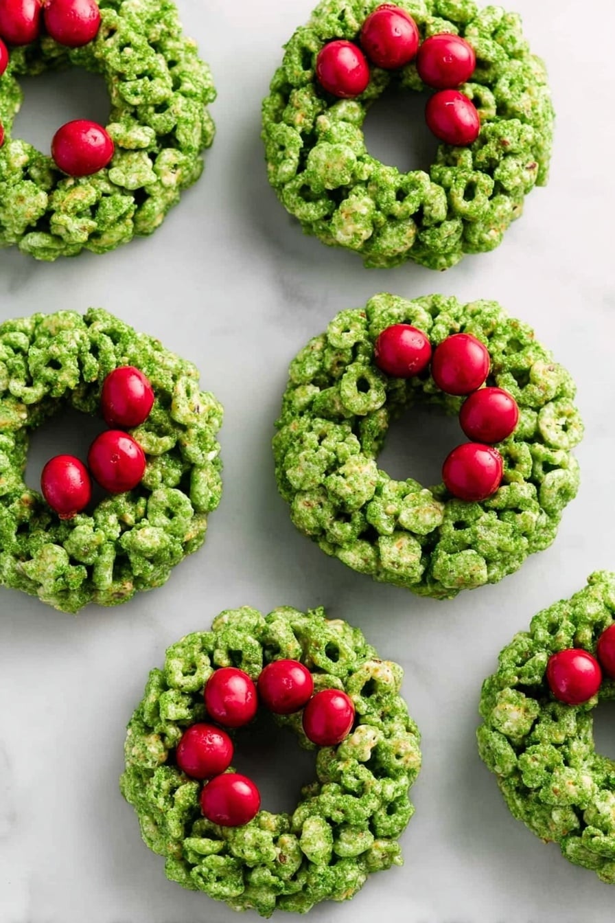 The image shows seven small green wreath-shaped treats placed on a white marbled surface. Each wreath is made from clusters of green cereal pieces stuck together, forming a thick ring with a hollow middle. Bright red round candies are grouped in threes on the top right side of each wreath, resembling berries on a holiday decoration. The green cereal has a rough texture with some visible cornflakes, and the red candies look smooth and shiny. The overall look is festive and colorful, with the wreaths evenly spaced across the surface. photo taken with an iphone --ar 2:3 --v 7 - Easy Cornflake Wreaths, Christmas snack ideas, holiday treats for kids, festive no-bake desserts, quick Christmas cookies