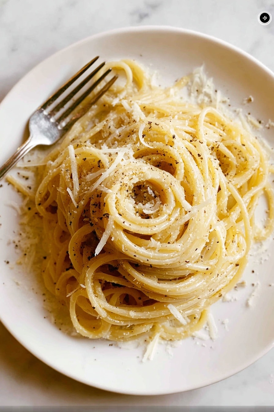 A white round plate holds a neatly twirled mound of spaghetti pasta as the main layer, pale yellow in color with a slight shine. Scattered over the pasta are small, irregular shreds of white cheese that add texture and light contrast to the smooth noodles. Black pepper flakes are sprinkled lightly, creating small dark spots across the dish. To the left side of the plate, a silver fork is partially visible, resting beside the pasta. The background has a white marbled texture, creating a clean and simple setting. Photo taken with an iphone --ar 2:3 --v 7 - Cacio e Pepe Pasta, Italian pasta recipes, easy pasta dishes, quick weeknight dinners, creamy cheese pasta