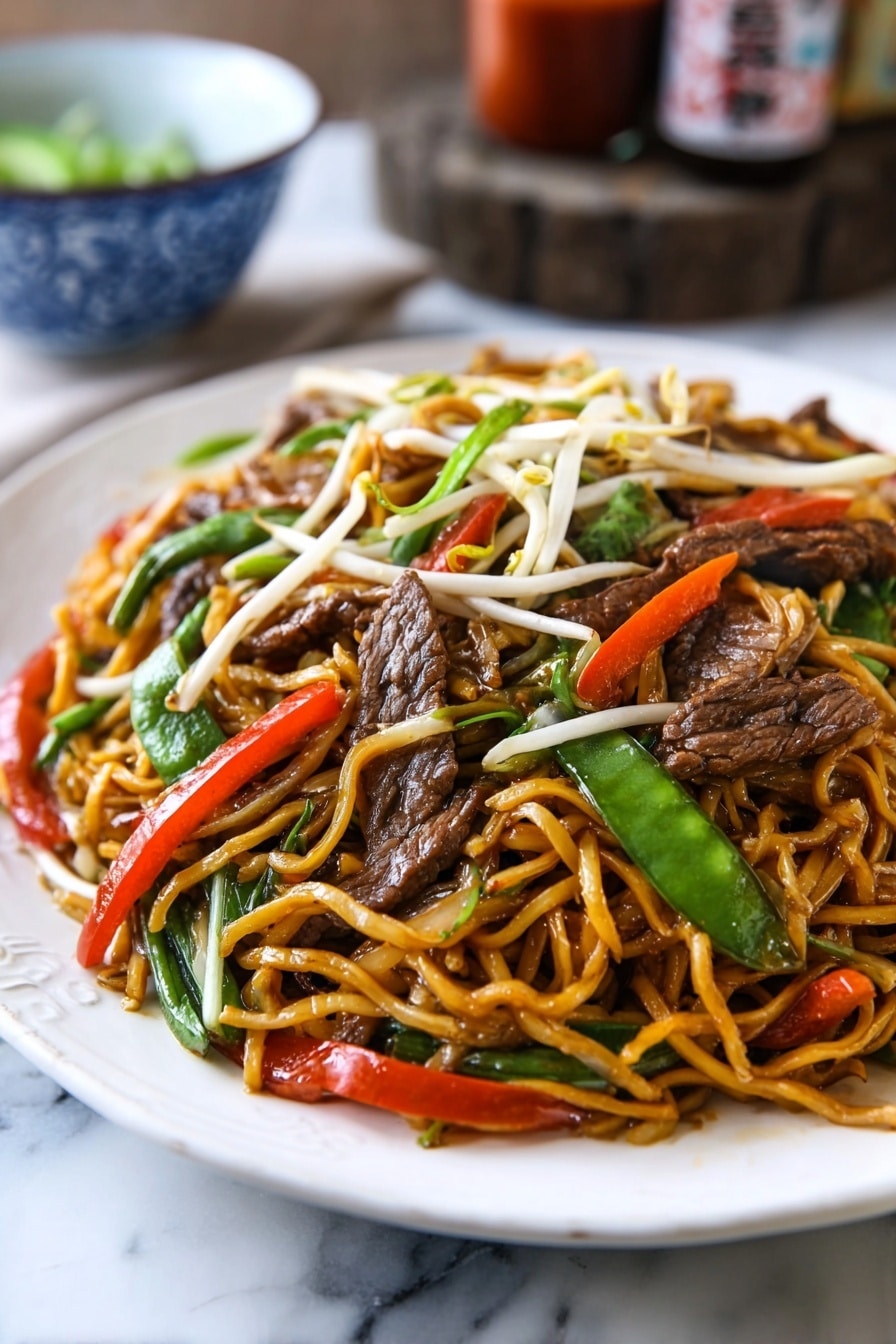 A white oval plate is filled with stir-fried noodles that are light brown and glossy, mixed with slices of dark brown beef, bright green snow peas, thin red chili strips, white bean sprouts, and pieces of translucent onion. The noodles are twisted and piled up high on the plate, with colorful vegetables and beef evenly spread throughout. The plate sits on a rustic wooden surface, with a blue cloth partially visible under one side. In the background, there are two brown bottles with red labels and a white bowl with blue patterns. photo taken with an iphone --ar 2:3 --v 7 - Beef Lo Mein Stir-Fry, Beef Lo Mein recipe, Chinese beef stir-fry, easy lo mein noodles, flavorful stir-fry dishes