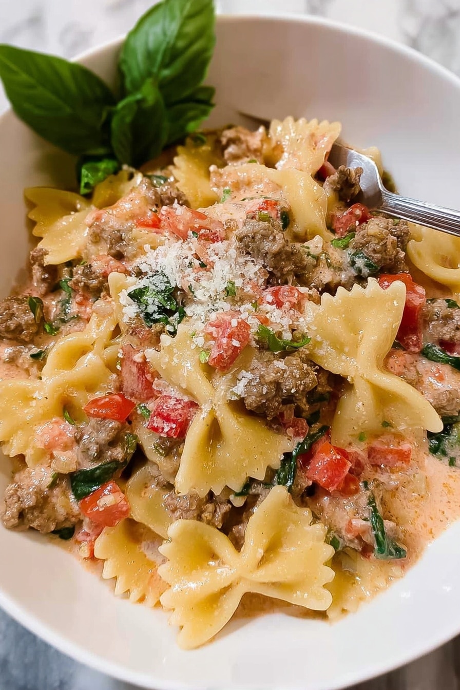 This image shows a black frying pan with creamy pasta inside. The pasta is bow-tie shaped with a light yellow color. Mixed in are small pieces of cooked ground meat, soft diced red tomatoes, and chopped green herbs scattered on top. The creamy sauce looks smooth and light orange, covering the pasta and ingredients evenly. The pan sits on a stove with visible black grates and control knobs in the background. Photo taken with an iphone --ar 2:3 --v 7 - Creamy Italian Sausage Bow Tie Pasta, Italian sausage pasta recipe, creamy sausage pasta, quick Italian dinner, easy pasta recipes