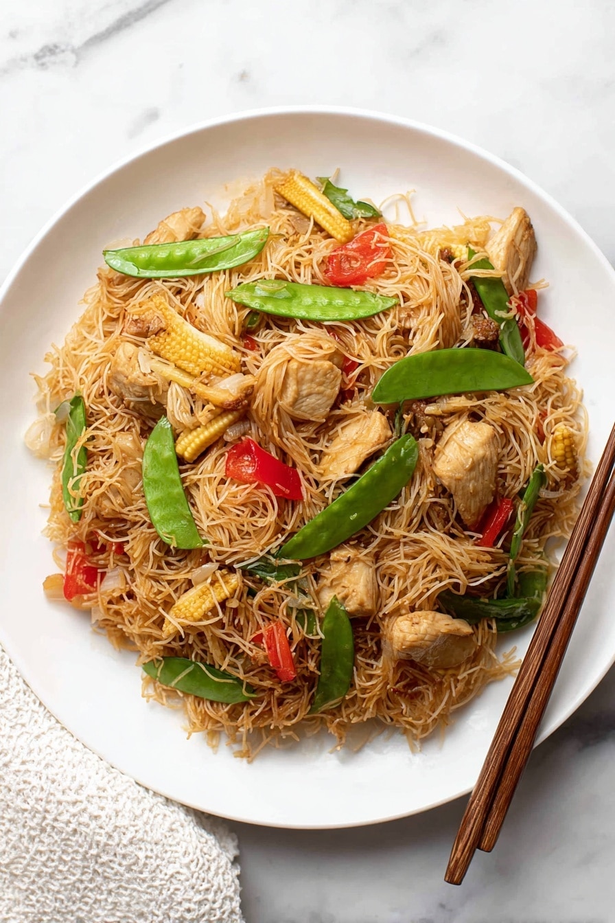 The dish shows a single layer of thin brown rice noodles mixed with pieces of light brown cooked chicken, small baby corn slices, bright green snap peas, red bell pepper slices, and bits of translucent cooked onion on a white plate. The plate is placed on a white marbled surface. To the right of the plate, there are two brown wooden chopsticks resting diagonally. A white textured cloth is partially visible at the bottom left corner of the image. photo taken with an iphone --ar 2:3 --v 7 - Singapore Curry Noodles Chinese stir-fry, easy curry noodle dish, quick Asian noodle recipe, flavorful curry noodle dinner, weeknight Asian meal