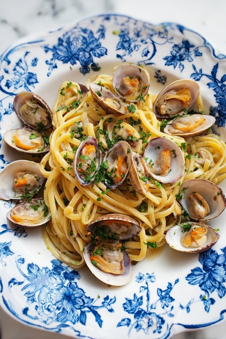A white plate with blue floral patterns holds a serving of spaghetti pasta as the bottom layer, light yellow and slightly shiny. On top of the pasta, there are many open clam shells with light brown and white inner textures and soft orange clam meat inside. The dish is sprinkled with finely chopped green parsley evenly over the pasta and clams. The plate is placed on a white marbled surface. photo taken with an iphone --ar 2:3 --v 7 - Linguine with Clams, Italian seafood pasta, easy clam pasta recipe, fresh clam pasta, seafood linguine