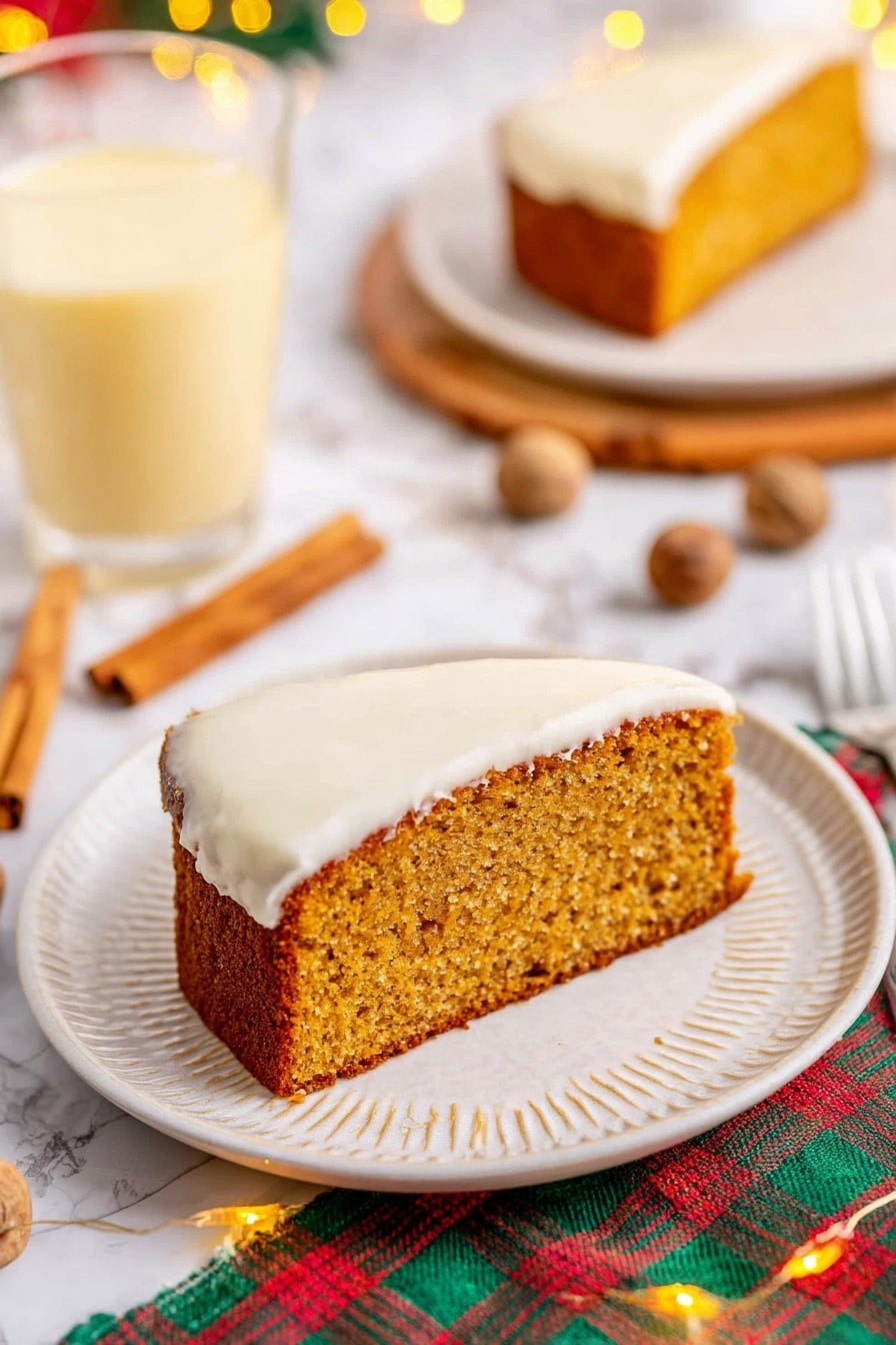 The image shows a single slice of moist, golden-brown cake with a thick layer of smooth white frosting on the bottom side, sitting on a white plate with a subtle textured rim. The cake slice has a slightly rough texture on top, indicating it is soft inside. Around the plate, there are cinnamon sticks and whole nutmegs scattered on a white marbled surface, with a colorful plaid cloth partially visible underneath. In the background, there is a clear glass filled with a light yellow creamy drink, and a second plate holding another slice of the same cake. Small warm fairy lights add a cozy touch to the scene. Photo taken with an iphone --ar 2:3 --v 7 - Eggnog Bread with Rum Extract, holiday eggnog bread recipes, festive holiday bread, spiced eggnog bread, rum extract holiday baking