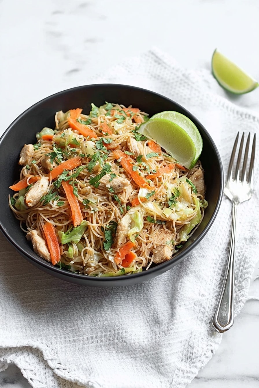 A black bowl sits on a white marbled surface with a white cloth beneath it, filled with thin light brown noodles mixed with small pieces of light beige chicken, bright orange carrot sticks, light green cabbage, and some fresh green herbs scattered on top. A half lime with a pale green inside rests on the right edge of the bowl. To the right of the bowl are a silver spoon and fork placed on the white marbled surface. photo taken with an iphone --ar 2:3 --v 7 - Easy Chicken and Pork Pancit Noodles, Filipino Pancit Noodles, Quick Chicken and Pork Stir-fry, Delicious Filipino Noodle Dish, Simple Filipino Recipes