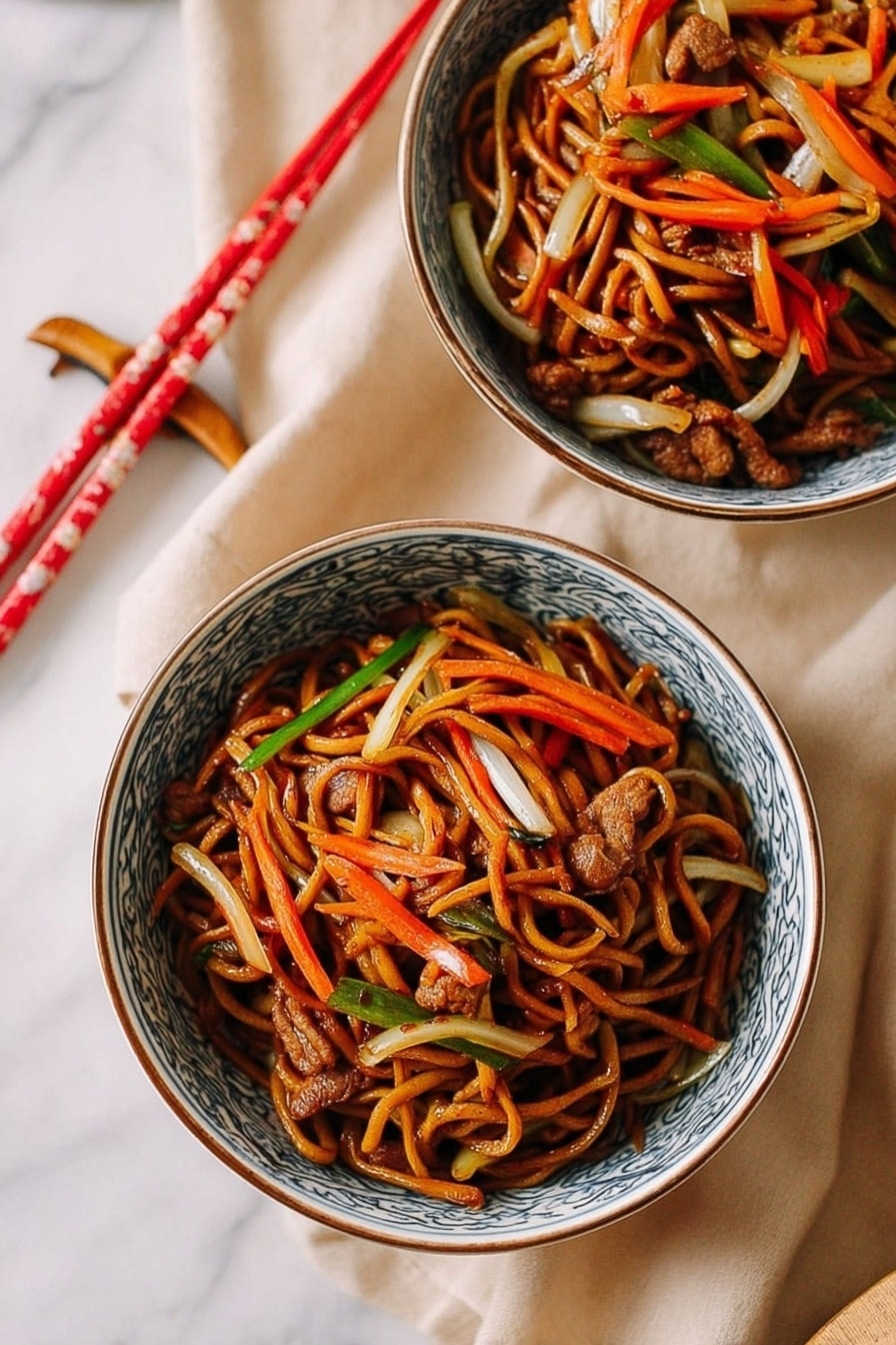 Two white bowls with blue patterns on the edges hold a serving of stir-fried noodles. The dish has multiple layers: a base of dark brown soy-coated noodles entwined with thin strips of orange carrots, white onions, and light green vegetables. Small pieces of cooked brown meat are scattered throughout. Both bowls are placed on a soft beige cloth on a white marbled surface. A pair of red and cream chopsticks rest near the bowls. photo taken with an iphone --ar 2:3 --v 7 - Restaurant-Style Chicken Lo Mein, Chicken Lo Mein recipe, Chinese chicken noodles, homemade lo mein, easy Chinese stir-fry