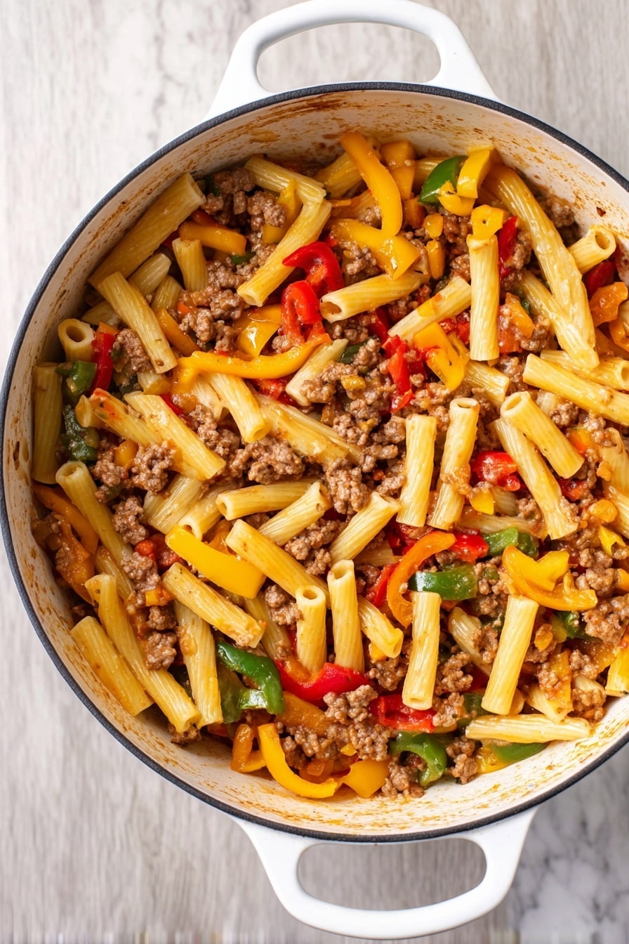 This image shows a white pot filled with a pasta dish featuring about three layers of ingredients. The bottom layer is short, tube-shaped pasta in a light yellow color. On top of this, there are chunks of cooked ground meat scattered throughout, appearing brown and crumbly. The top layer is mixed vegetables, including strips of red, yellow, and green bell peppers, adding bright colors and a fresh texture. The pot has white handles and sits on a white marbled surface. Photo taken with an iphone --ar 2:3 --v 7 - Italian Sausage and Peppers Pasta, Italian Sausage Pasta, easy sausage pasta recipe, quick weeknight dinner, flavorful pasta dishes