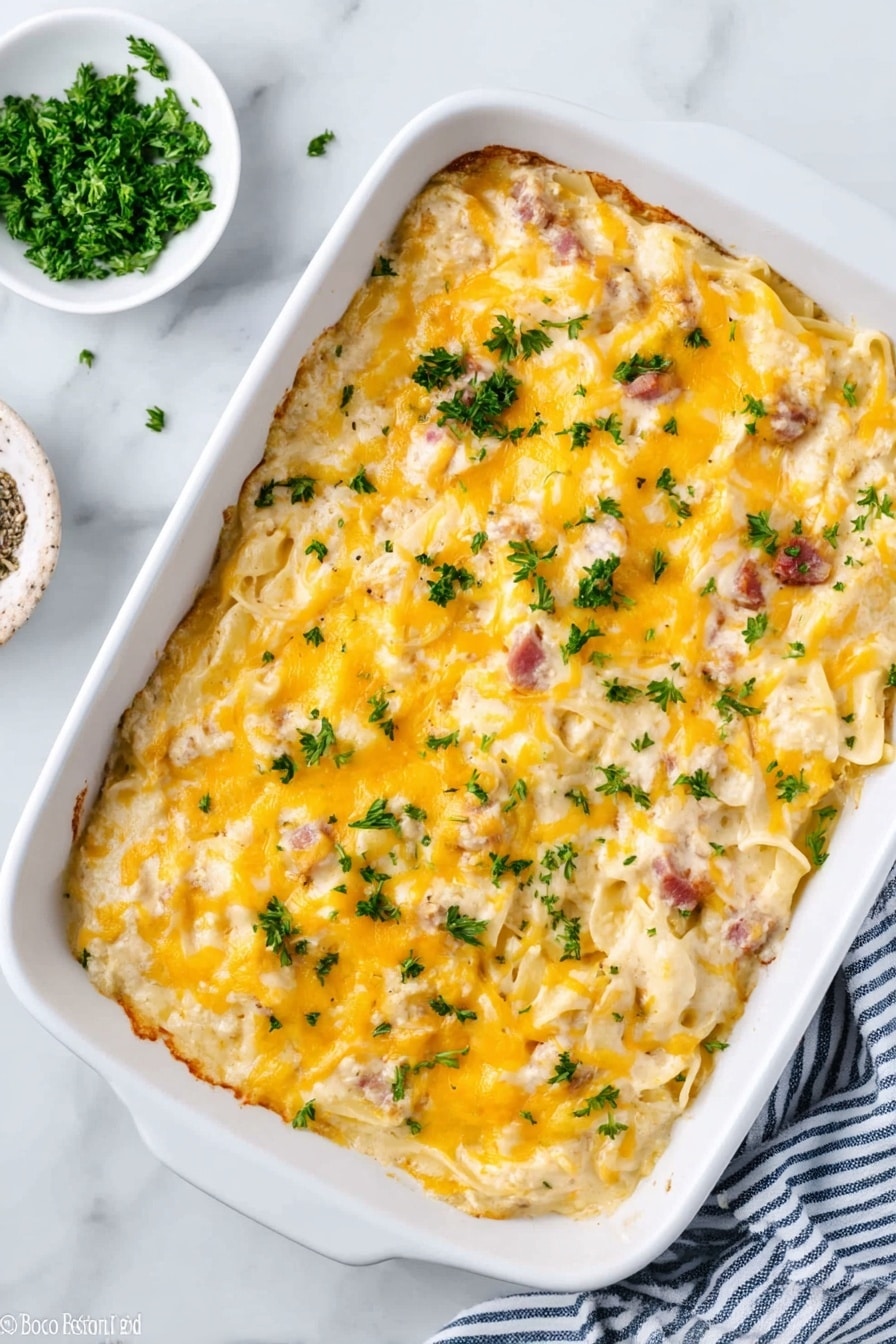 In the image, there is a white rectangular baking dish filled with creamy pasta that has a thick layer of melted yellow cheese on top. The pasta is visible under the cheese, showing a mix of white noodles and small pieces of light brown and pinkish ingredients, likely meat. Fresh green herbs are sprinkled over the cheese, adding a touch of color. The dish sits on a white marbled surface, with a small white bowl of chopped green herbs placed to the side and a blue and white striped cloth nearby. The top of the pasta has a slightly shiny texture from the cheese. Photo taken with an iphone --ar 2:3 --v 7 - Cheesy Chicken Spaghetti Bake, chicken spaghetti casserole, cheesy pasta bake, easy chicken pasta dinner, comfort food recipes