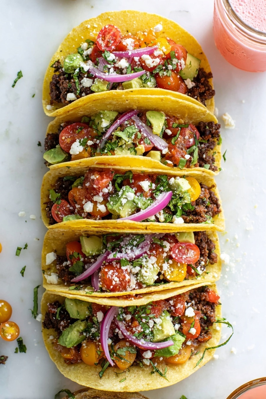 Four soft yellow corn tacos are stacked vertically over a white marbled surface. Each taco has a base layer of crumbled dark brown seasoned ground meat, topped with a colorful salad mix of chopped red and yellow cherry tomatoes, green avocado chunks, and fresh green cilantro. Thin slices of bright purple-red onions curve on top, with some white crumbly cheese sprinkled in between the layers. To the upper right, a small glass jar with a pink drink is partially visible. The scene is bright and fresh, showing vibrant colors and textures. photo taken with an iphone --ar 2:3 --v 7 - Easy Ground Beef Tacos, ground beef tacos, quick taco dinner, homemade taco filling, best beef taco recipe