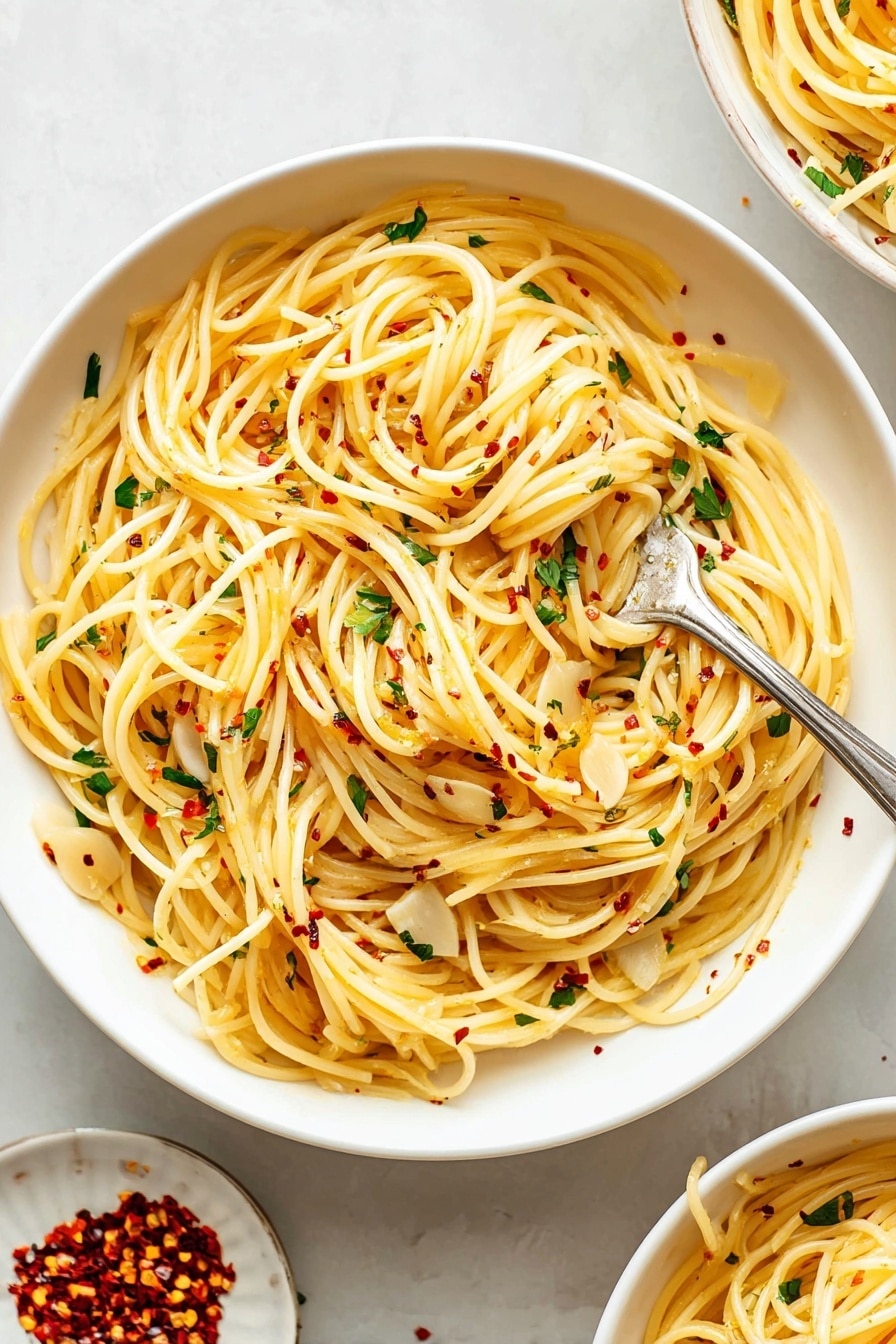 A large white bowl filled with long, thin spaghetti noodles that are lightly coated with olive oil, giving them a soft yellow color. Scattered throughout the pasta are thin, flat slices of garlic and small bits of fresh green parsley. Tiny red chili flakes are sprinkled evenly on top, adding small pops of red. A silver fork is twirling a small bundle of the pasta near the center of the bowl. The bowl rests on a white marbled surface, with a small white plate next to it containing additional red chili flakes. Part of another similar bowl filled with the same pasta can be seen in the upper right corner. Photo taken with an iphone --ar 2:3 --v 7 - Spaghetti Aglio e Olio, Italian pasta recipes, quick dinner ideas, garlic pasta, easy Italian main dish