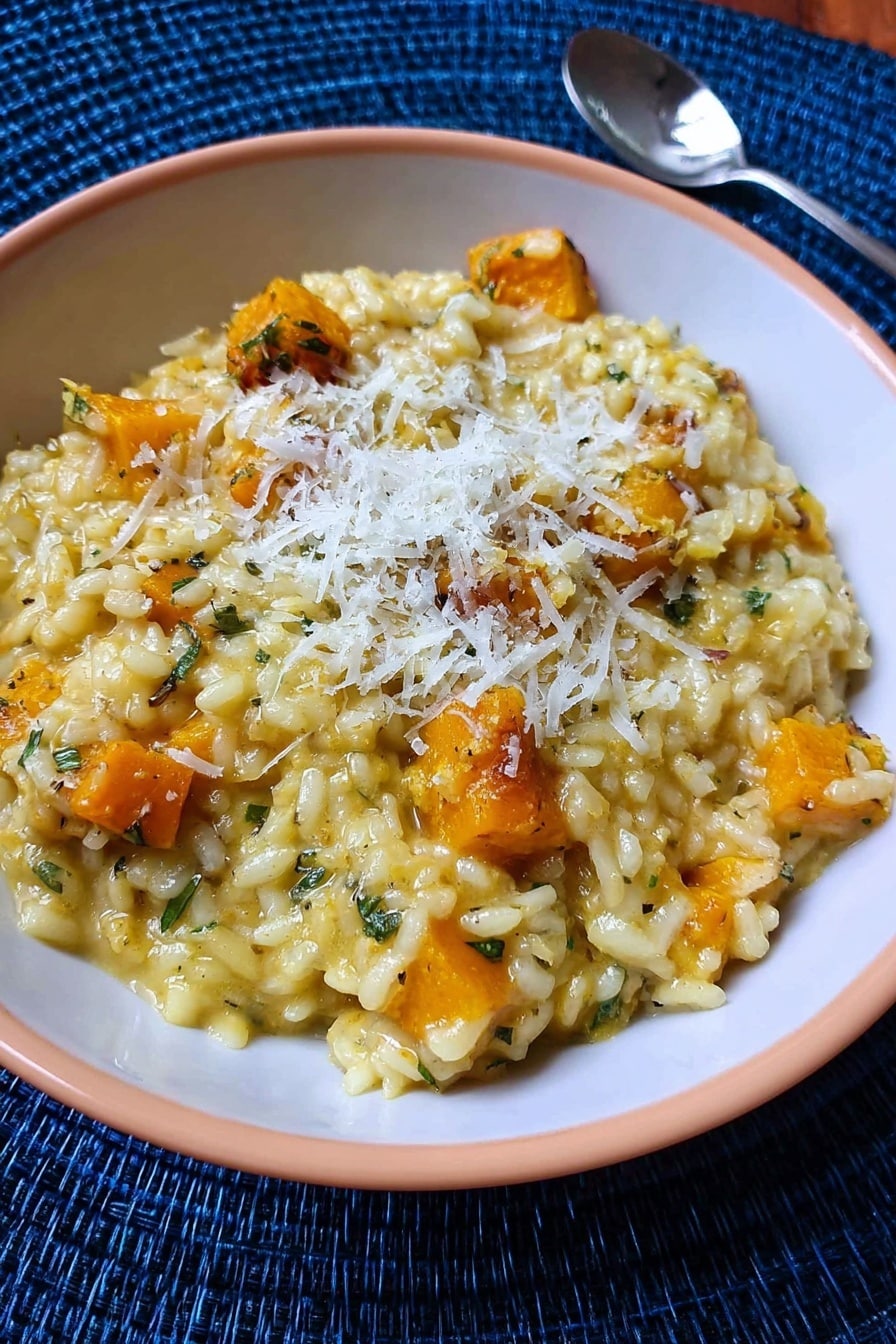 A white plate with blue patterns holds a layer of creamy yellow risotto with soft, slightly shiny grains and some orange pieces mixed inside. On top, there is a thick, juicy piece of cooked meat with a browned surface and visible herbs. A small green sprig of rosemary lies between the risotto and meat, adding fresh color. The plate is set against a white marbled background. photo taken with an iphone --ar 2:3 --v 7 - Butternut Squash Risotto with Saffron, butternut squash risotto, saffron risotto recipe, creamy squash risotto, easy vegetarian risotto
