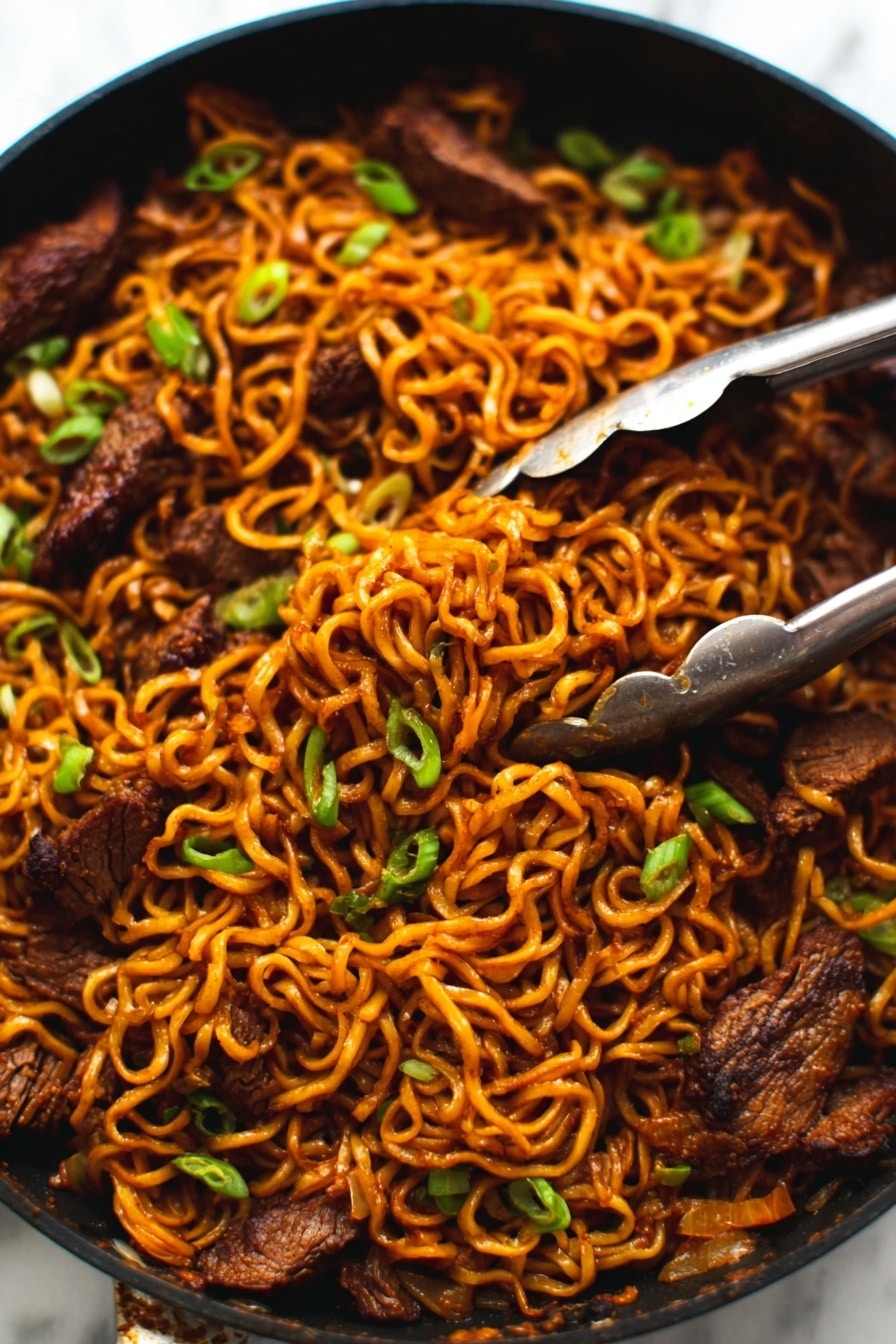 The image shows a close-up of a black pan filled with cooked noodles mixed with pieces of dark brown meat. The noodles are a warm orange-brown color, twisted and tangled together with small green onions sprinkled on top for color contrast. A pair of silver tongs is gripping some noodles and meat in the top right area of the pan. The pan sits on a white marbled surface. photo taken with an iphone --ar 2:3 --v 7 - Spicy Korean Beef Noodles, Korean Beef Noodles recipe, spicy noodle bowl, Korean beef stir-fry, quick Korean dinner