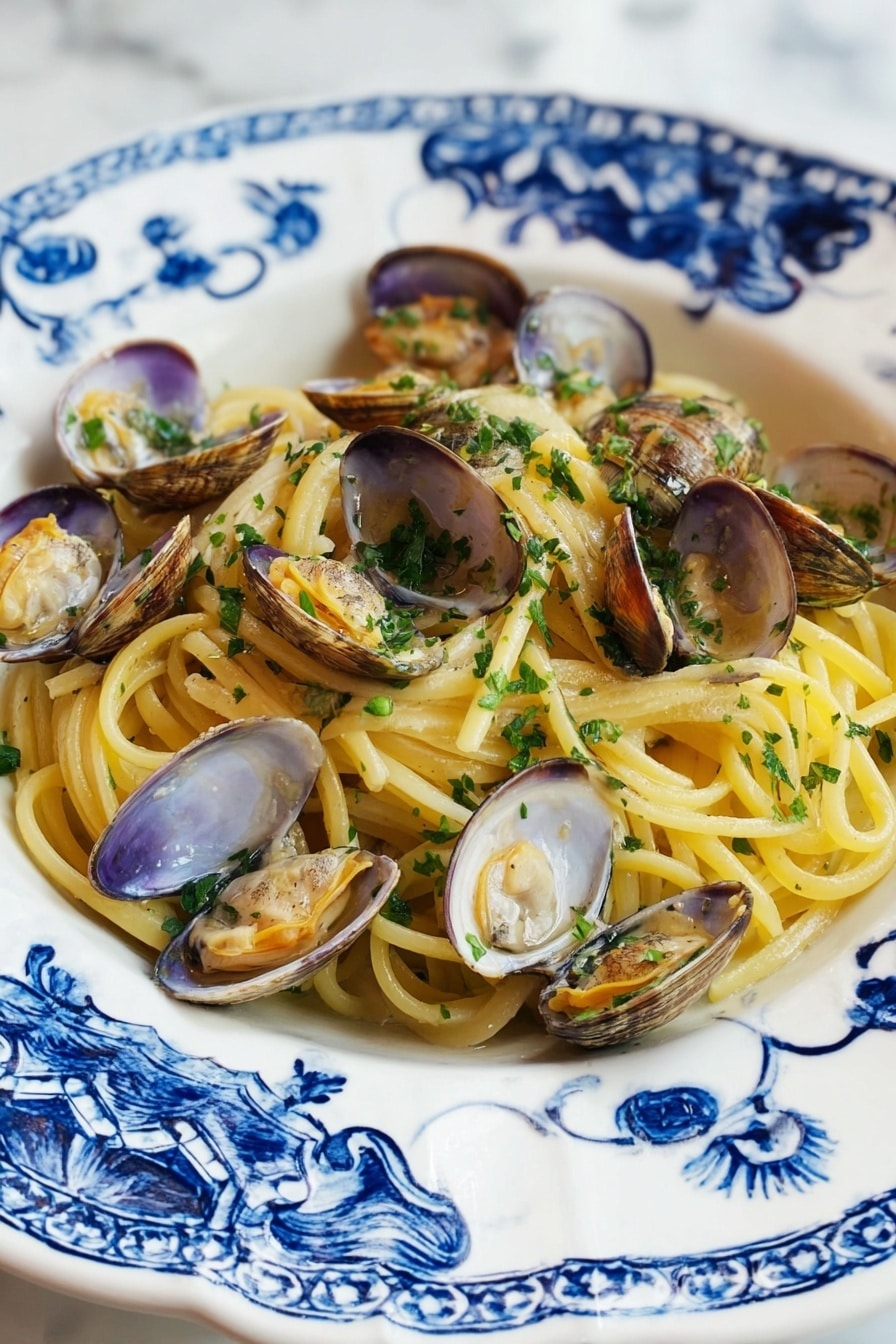 A white plate with blue floral patterns holds a serving of spaghetti pasta layered at the bottom, showing a pale yellow color and smooth texture. Scattered over the pasta are many opened clam shells, beige and light brown with tender clam meat inside, slightly orange and shiny. Fresh chopped green herbs are sprinkled over the clams and pasta, adding a bright touch. The plate rests on a white marbled surface. photo taken with an iphone --ar 2:3 --v 7 - Linguine with Clams, Italian seafood pasta, easy clam pasta recipe, fresh clam pasta, seafood linguine