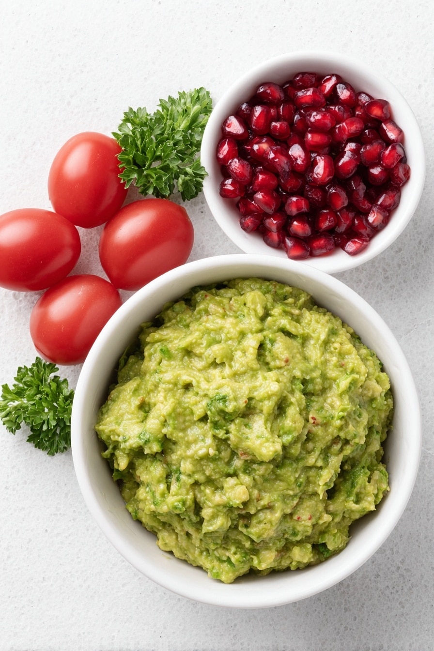 Flat lay of a simple white ceramic bowl filled with fresh green guacamole, a small white bowl containing bright red pomegranate seeds, a cluster of ripe red cherry tomatoes, and a few vibrant green sprigs of parsley placed neatly around the bowls, all arranged with perfect symmetry and balanced proportions, placed on a clean white marble surface, soft natural light, photo taken with an iPhone, professional food photography style, fresh ingredients, white ceramic bowls, no bottles, no duplicates, no utensils, no packaging --ar 2:3 --v 7 --p m7354615311229779997 - Festive Guacamole with Pomegranate & Tomatoes, holiday guacamole recipe, easy party dip, colorful fruit guacamole, quick festive appetizer