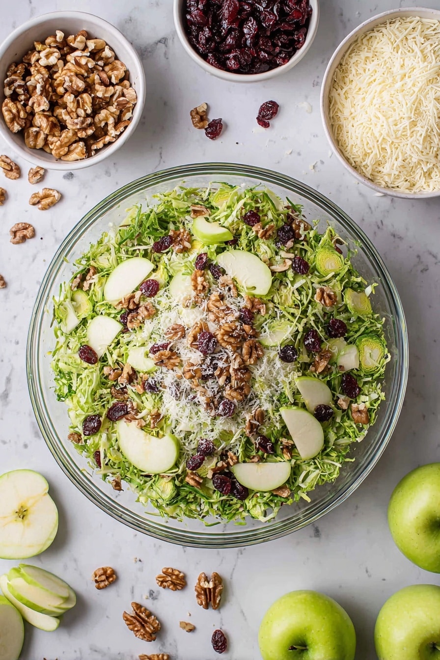 A large clear glass bowl filled with a fresh salad showing three layers: the bottom layer is shredded green Brussels sprouts, the middle layer is thinly sliced green apple slices placed evenly around, and the top layer is scattered walnut pieces, dark red dried cranberries, and small white grated cheese bits, all on a white marbled surface. Around the bowl are small white bowls containing walnuts, grated cheese, and dried cranberries, along with whole and sliced green apples and loose salad leaves scattered nearby. Photo taken with an iphone --ar 2:3 --v 7 - Crispy Brussels Sprouts Salad with Apples, healthy Brussels sprouts salad, easy autumn salad, crunchy Brussels sprouts apple salad, flavorful vegetarian salad