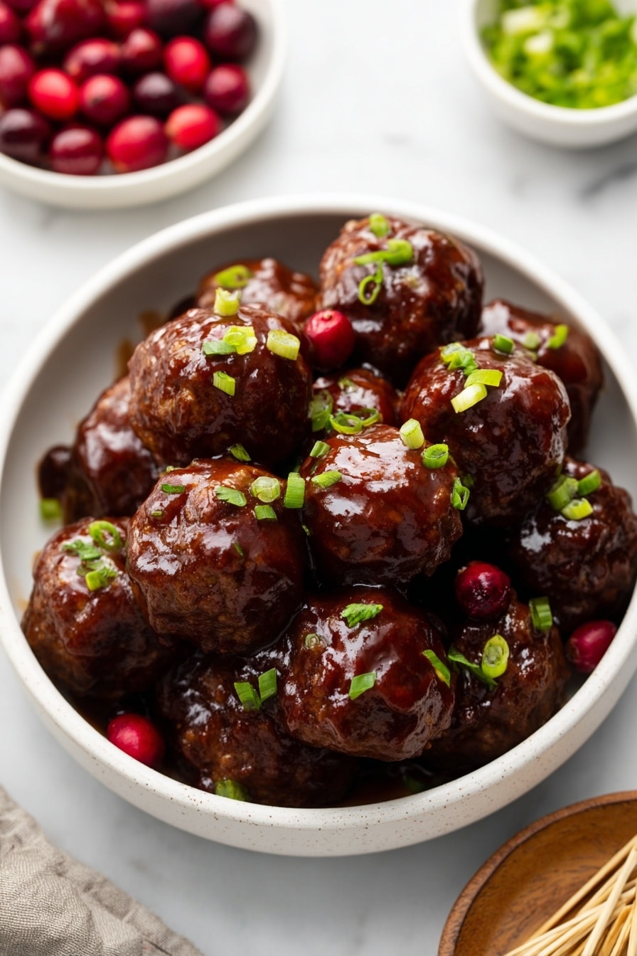 A white bowl filled with eight dark brown meatballs covered in glossy, thick sauce. The meatballs are round and uneven in shape, arranged close together, with small bright green chopped scallions sprinkled on top. A few red cranberries are visible between the meatballs at the base. The bowl sits on a white marbled surface surrounded by small white bowls of cranberries, scallions, and wooden picks. Photo taken with an iphone --ar 2:3 --v 7 - Cranberry BBQ Turkey Meatballs, turkey meatball recipe, cranberry barbecue sauce, easy appetizer ideas, flavorful meatball recipes