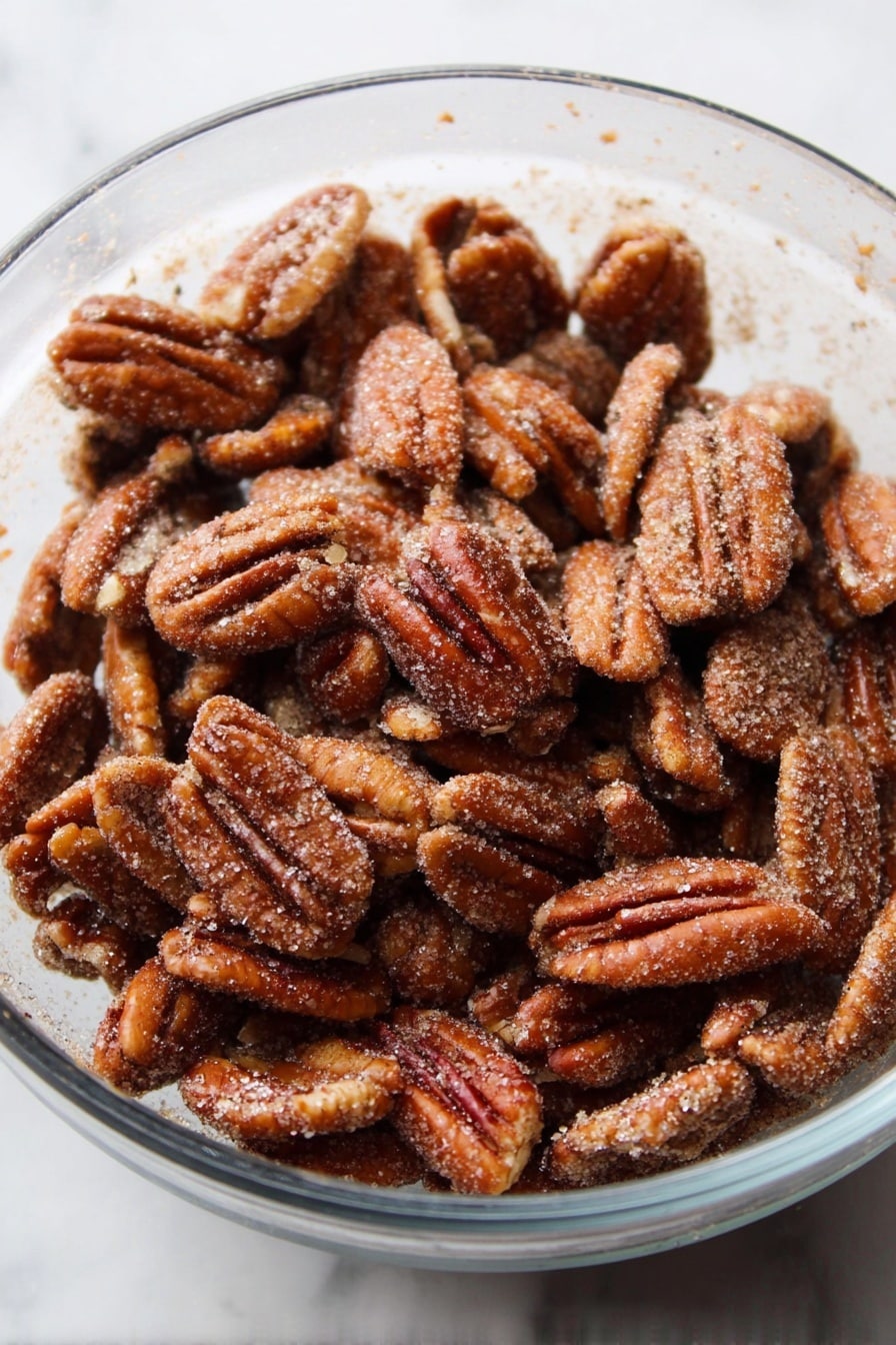 A clear glass bowl is full of many toasted pecan halves, each nut showing a rough, crinkled surface with a shiny brown color covered lightly with a layer of fine sugar crystals and cinnamon dust. The bowl sits on a white marbled surface. photo taken with an iphone --ar 2:3 --v 7 - Cinnamon Sugar Candied Pecans, candied pecans, sweet pecan snacks, crunchy pecan treats, homemade candied nuts