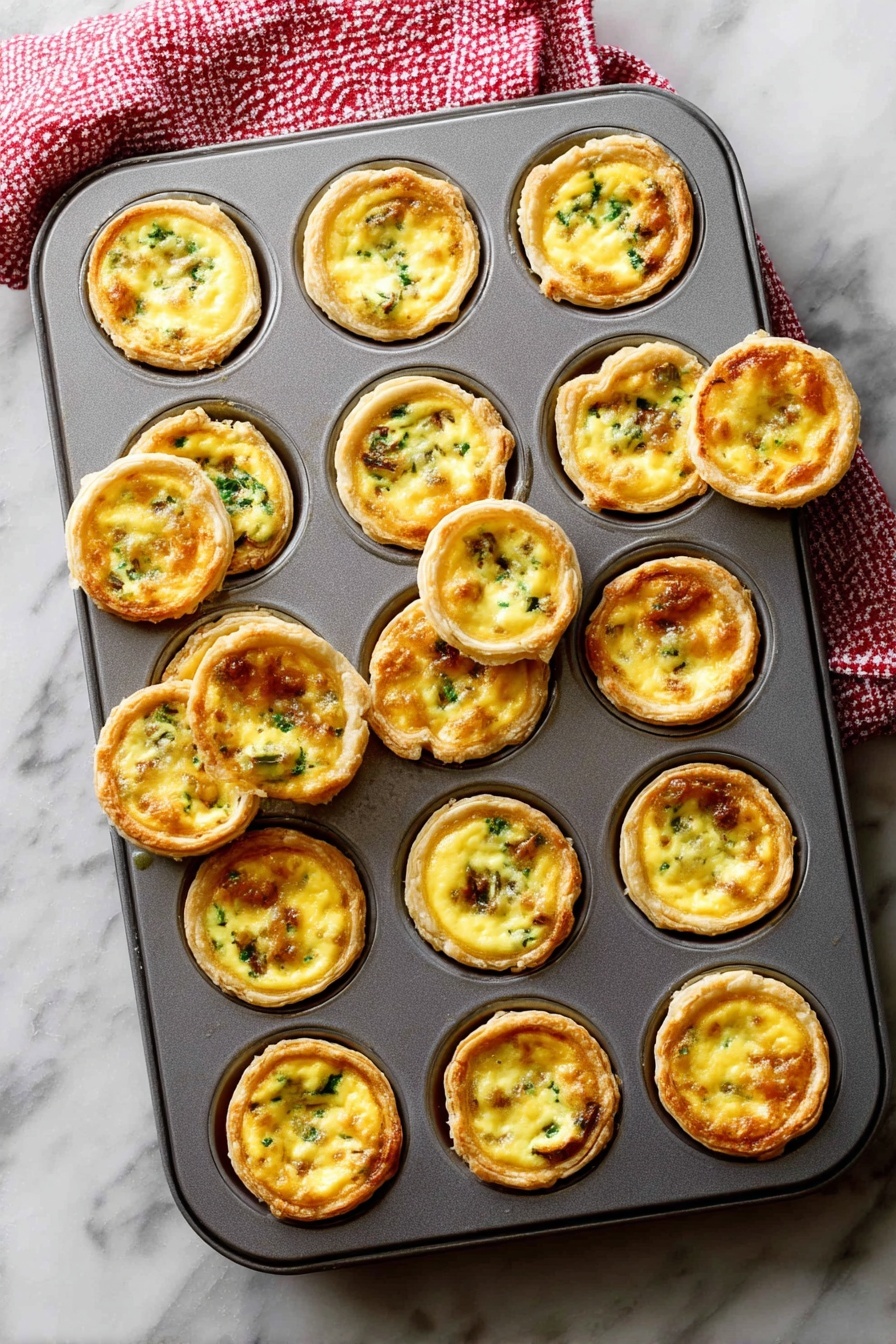 A gray metal muffin tray filled with 24 mini egg tarts, each tart consisting of a golden brown crust that forms a cup holding a smooth, creamy yellow egg filling mixed with small green and brown bits of vegetables or meat. Some tarts are slightly raised above the tray’s edge, showing a crisp outer layer, while a few are tilted or removed, revealing their round, flaky textured bottoms. The tray rests on a white marbled surface with a red and white checkered towel partly visible at the top left corner. Photo taken with an iphone --ar 2:3 --v 7 - Mini Quiche Bites Flaky Pie Crust, mini quiche recipes, savory snack ideas, brunch finger foods, easy appetizer recipes