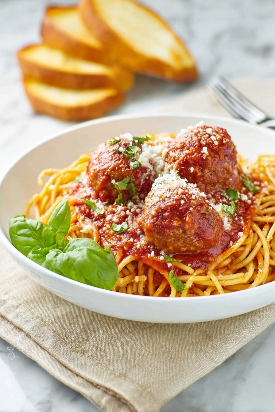 A white bowl holds a bed of golden-yellow spaghetti noodles topped with rich red tomato sauce. On top, there are three large brown meatballs coated in the sauce, sprinkled with white grated cheese and small green herb pieces. A fresh green basil leaf adds color near the front. In the background, there are three toasted bread slices leaning against the bowl. The scene sits on a beige cloth over a white marbled surface. A silver fork rests nearby on the right side. Photo taken with an iphone --ar 2:3 --v 7 - Homemade Spaghetti and Meatballs, Italian comfort food, homemade marinara, easy pasta recipes, classic meatball recipe