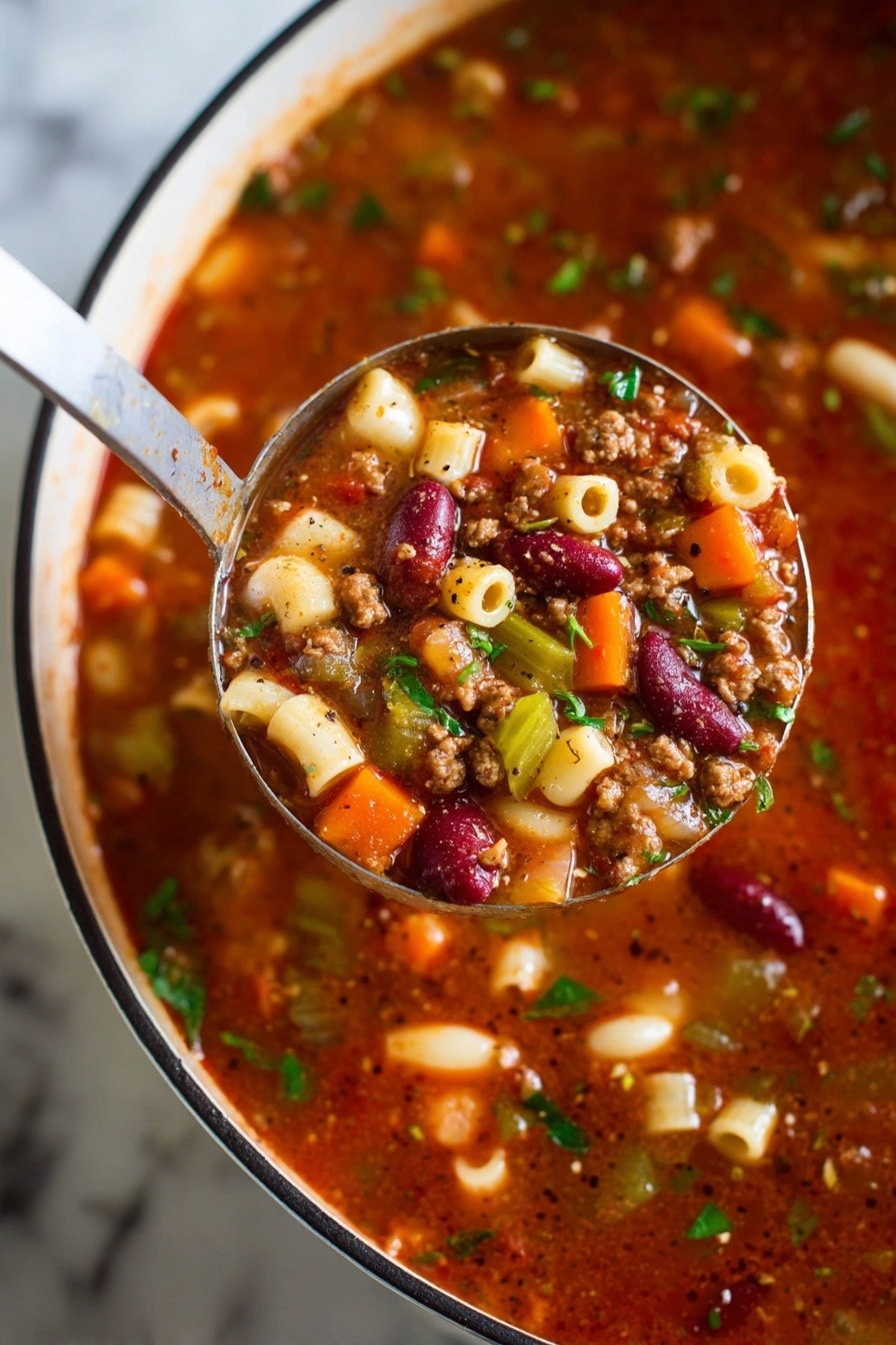 A close-up view of a ladle holding a rich, chunky soup above a white pot with a black rim, all resting on a white marbled surface. The soup has multiple layers visible: a thick, deep red broth base mixed with small bits of brown ground meat, bright orange carrot cubes, pale white and red kidney beans, green celery slices, and small round pasta pieces. Fresh green herbs are sprinkled throughout, adding a fresh touch. Black pepper flecks are visible on the surface of the soup and ladle, giving it a seasoned look. photo taken with an iphone --ar 2:3 --v 7 - Creamy Pasta e Fagioli Soup, Pasta e Fagioli soup, hearty vegetable and bean soup, creamy Italian soup, easy Pasta e Fagioli recipe