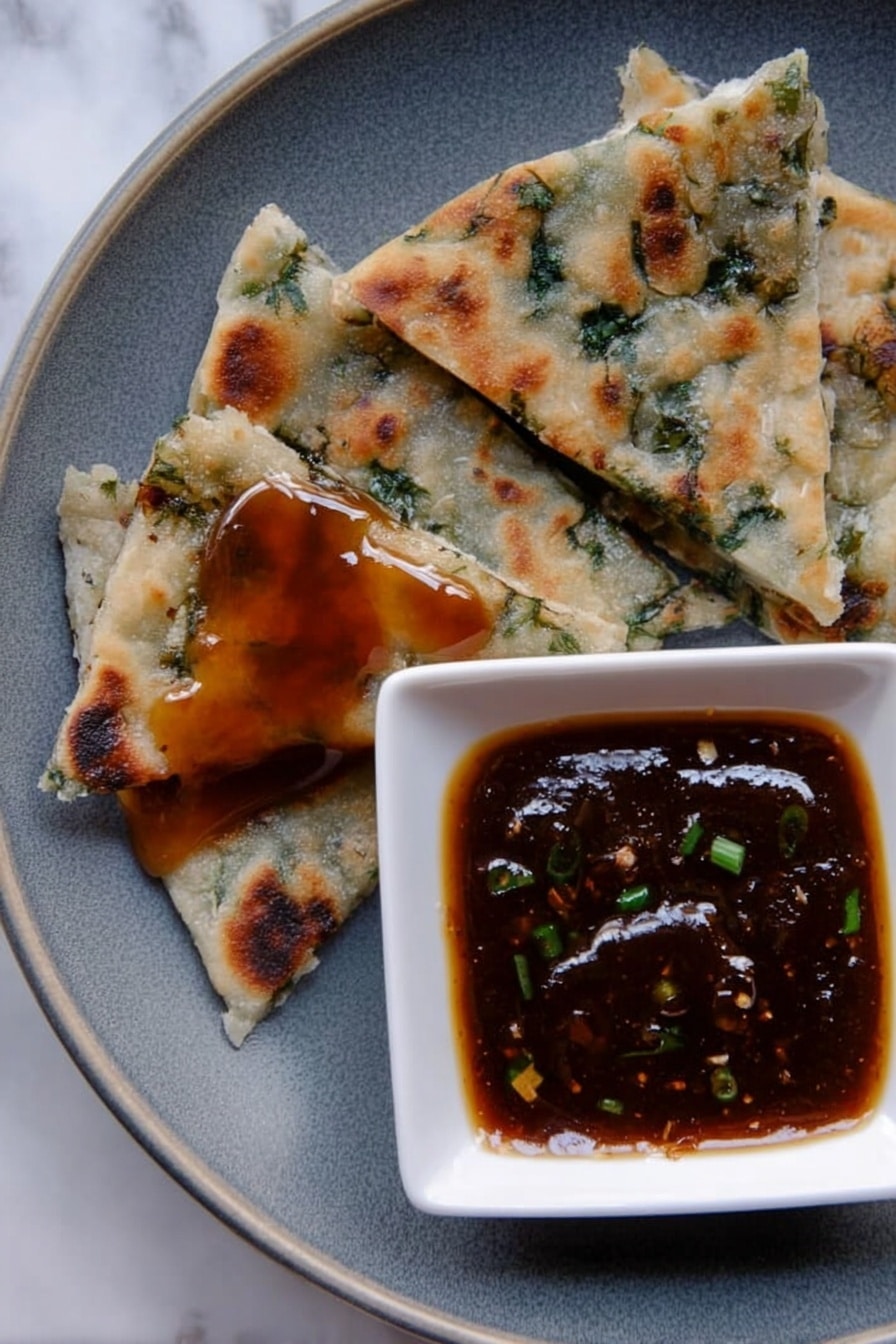 The image shows a close-up of a grey plate on a white marbled surface, with four triangular pieces of flatbread that have green herbs inside, each piece varying in size and texture with some browned spots from cooking. One piece near the bottom left has a shiny layer of sticky, dark amber sauce on top. To the right, a small white square bowl holds a thick, dark brown dipping sauce with small green bits inside, creating a glossy surface. photo taken with an iphone --ar 2:3 --v 7 - Chinese Scallion Pancakes, scallion pancake recipe, Chinese street food snacks, crispy scallion pancakes, easy Chinese pancakes