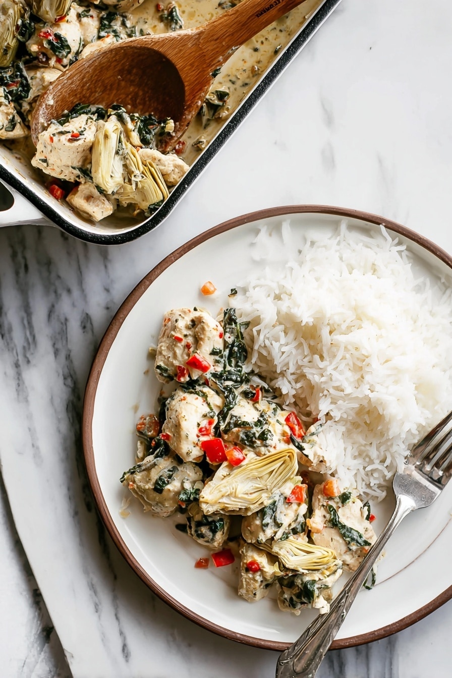 A white round plate shows two layers: on the left side, there are pieces of white cooked chicken mixed with dark green spinach leaves and small bright red bits of bell pepper, along with beige artichoke hearts placed among the chicken; on the right side, there is a mound of fluffy white rice with a silver fork resting on the right edge of the plate. Above the plate, a white rectangular baking dish with a dark rim holds more chicken mixture, and a wooden spoon is scooping some of the chicken and vegetables from the dish. All items are placed on a white marbled surface. photo taken with an iphone --ar 2:3 --v 7 - Spinach Artichoke Chicken Bake, chicken spinach artichoke bake, baked chicken with spinach and artichokes, easy chicken bake recipes, creamy vegetable chicken dish
