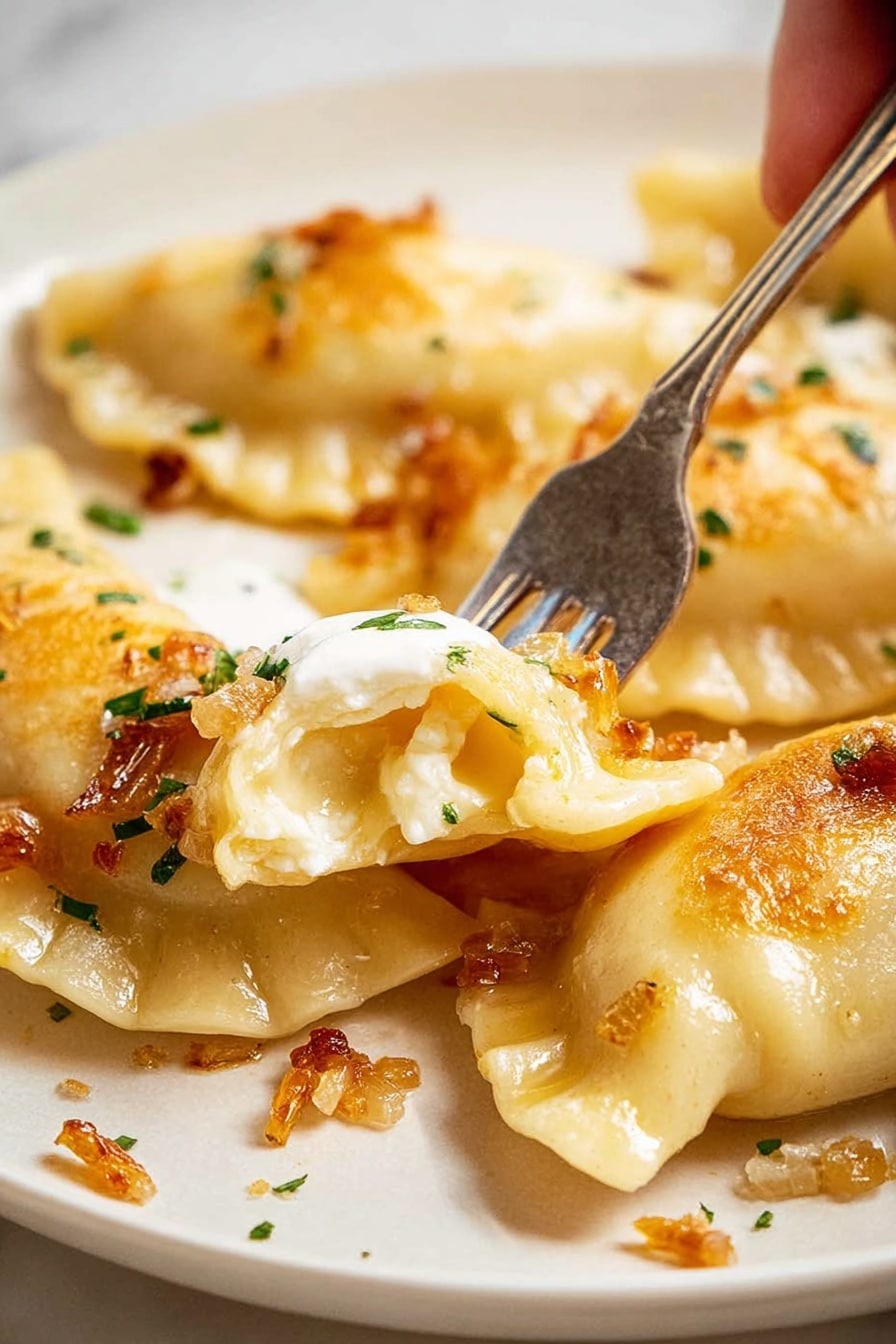 A close-up shot shows several golden brown pierogi with a soft, slightly crispy dough texture on a white plate. One pierogi is being pierced by a metal fork held by a woman's hand, revealing a creamy, pale yellow potato filling inside. The pierogi are lightly topped with small bits of golden fried onions and sprinkled with green herbs. There is a bit of white sour cream on top of the pierced pierogi, adding a creamy contrast. The white plate sits on a white marbled surface with small droplets and bits of fried onions around. photo taken with an iphone --ar 2:3 --v 7 - Cheesy Potato Pierogi Ruskies, Polish dumplings with cheese and potatoes, homemade pierogi filling recipes, traditional Polish pierogi, easy pierogi ideas