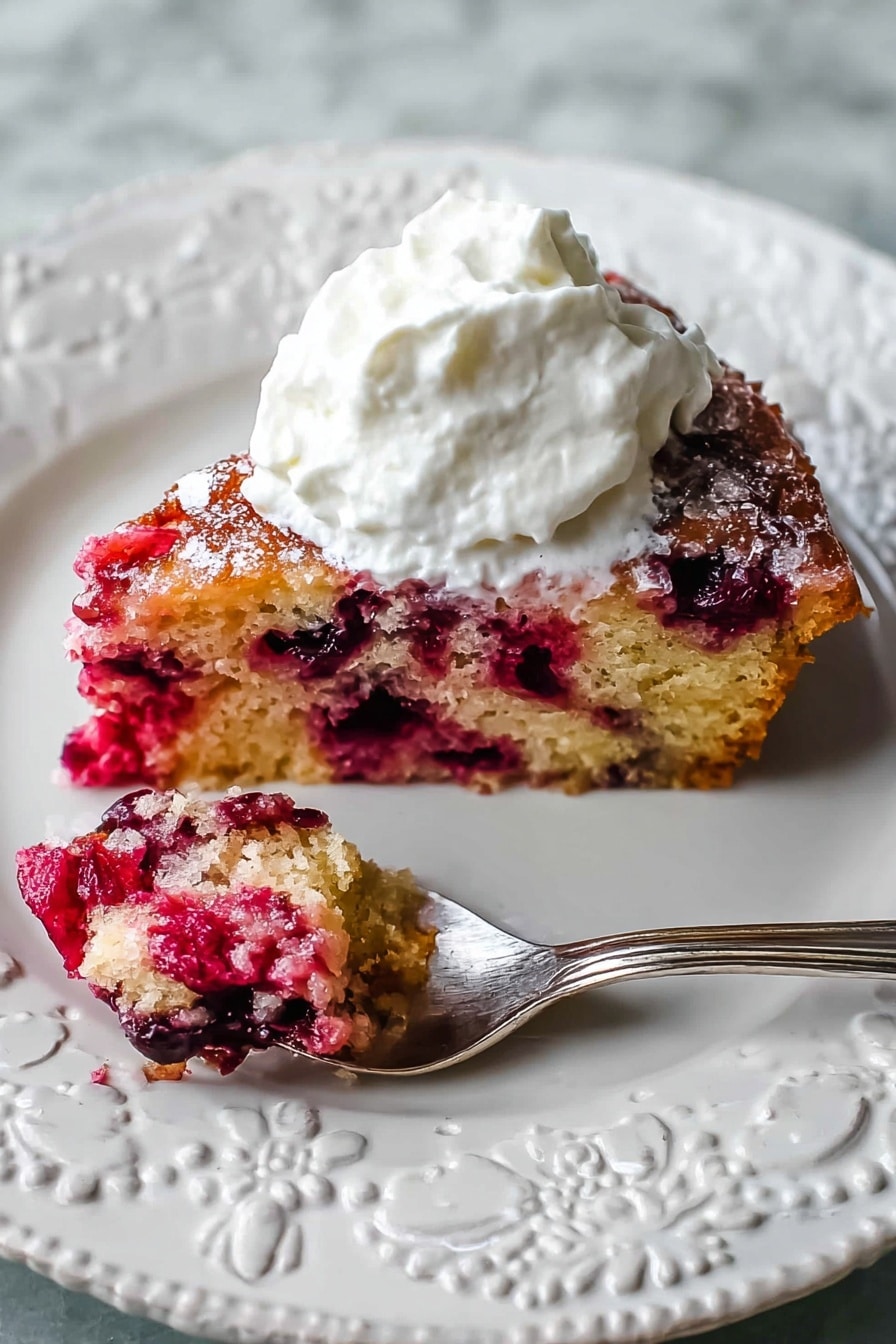 A slice of berry cake is placed on a white decorative plate with raised floral patterns. The cake has two visible layers: the bottom layer is a light golden-brown sponge filled with bright red and dark purple berries throughout, while the top layer appears slightly caramelized with a glossy texture and scattered sugar crystals. A generous dollop of fluffy white whipped cream sits on top of the cake. To the left of the cake, a silver spoon holds a small bite of the berry cake, showing its moist and chunky berry-filled texture. The plate rests on a white marbled surface photo taken with an iphone --ar 2:3 --v 7 - Cranberry Nut Cake, Cranberry Nut Cake recipe, festive holiday cake, moist cranberry dessert, nutty cake with cranberries