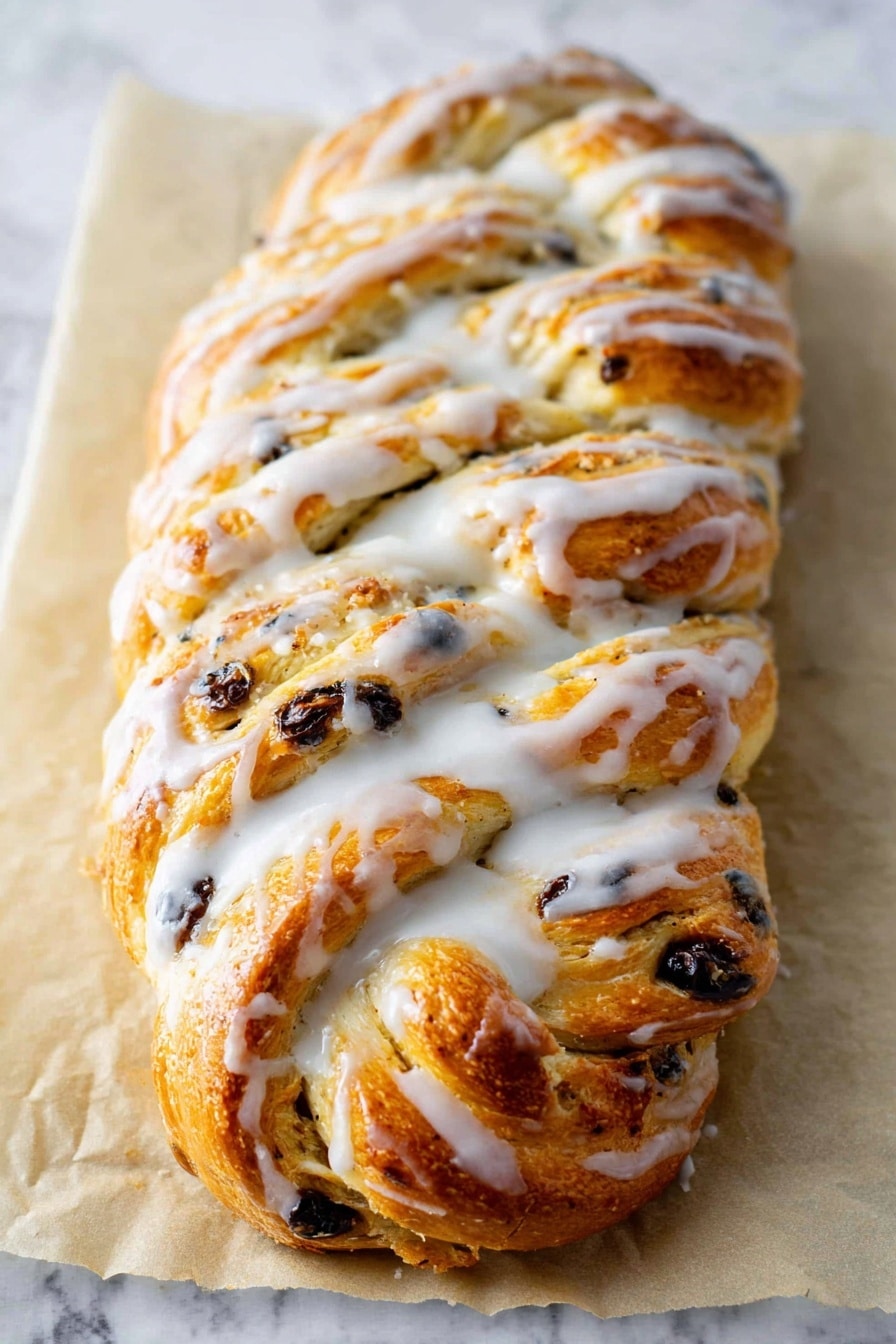 A golden brown braided bread loaf is placed on a sheet of parchment paper on a white marbled surface. The bread has multiple visible layers formed by the braid, with bits of dark raisins or chocolate chips scattered throughout the dough. A thick, white glaze is drizzled generously and unevenly over the top, pooling slightly in the crevices and along the edges, giving it a shiny, slightly wet look. The texture of the bread appears soft and fluffy with a slightly crisp crust on top. Photo taken with an iphone --ar 2:3 --v 7 - German Stollen Bread, festive German bread, Christmas fruit bread, traditional German Stollen, holiday bread recipes