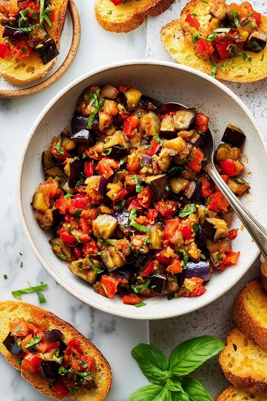 A white bowl filled with a colorful mix of roasted vegetables, mostly deep purple eggplants and bright red bell peppers, chopped into small pieces and mixed with finely chopped green herbs sprinkled on top. A silver spoon rests inside the bowl with its handle leaning on the edge. Around the bowl, there are toasted slices of bread topped with the same vegetable mix, placed on a white marbled surface. Fresh green basil leaves add a pop of color near the bowl. The overall look is fresh and vibrant, with a mix of soft cooked texture and crunchy toasted bread. photo taken with an iphone --ar 2:3 --v 7 - Eggplant Caponata, Mediterranean Eggplant Appetizer, Sicilian Eggplant Dish, Vegan Eggplant Snack, Tangy Eggplant Side Dish