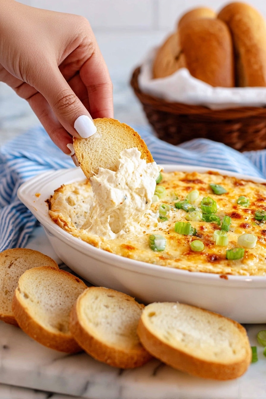 The image shows a white oval dish filled with a creamy, cheesy dip that has a golden brown top layer sprinkled with green chopped scallions. A woman's hand with white nail polish is holding a slice of light brown toasted bread, dipping into the soft, white cheese layer underneath. Several slices of the toasted bread are laid out in front of the dish on a white marbled surface with a blue and white striped cloth underneath. In the background, a blurred brown basket filled with bread is visible. Photo taken with an iphone --ar 2:3 --v 7 - Cheesy Roasted Cauliflower Dip, cheesy cauliflower dip, roasted cauliflower appetizer, healthy cauliflower dip, creamy vegetable dip