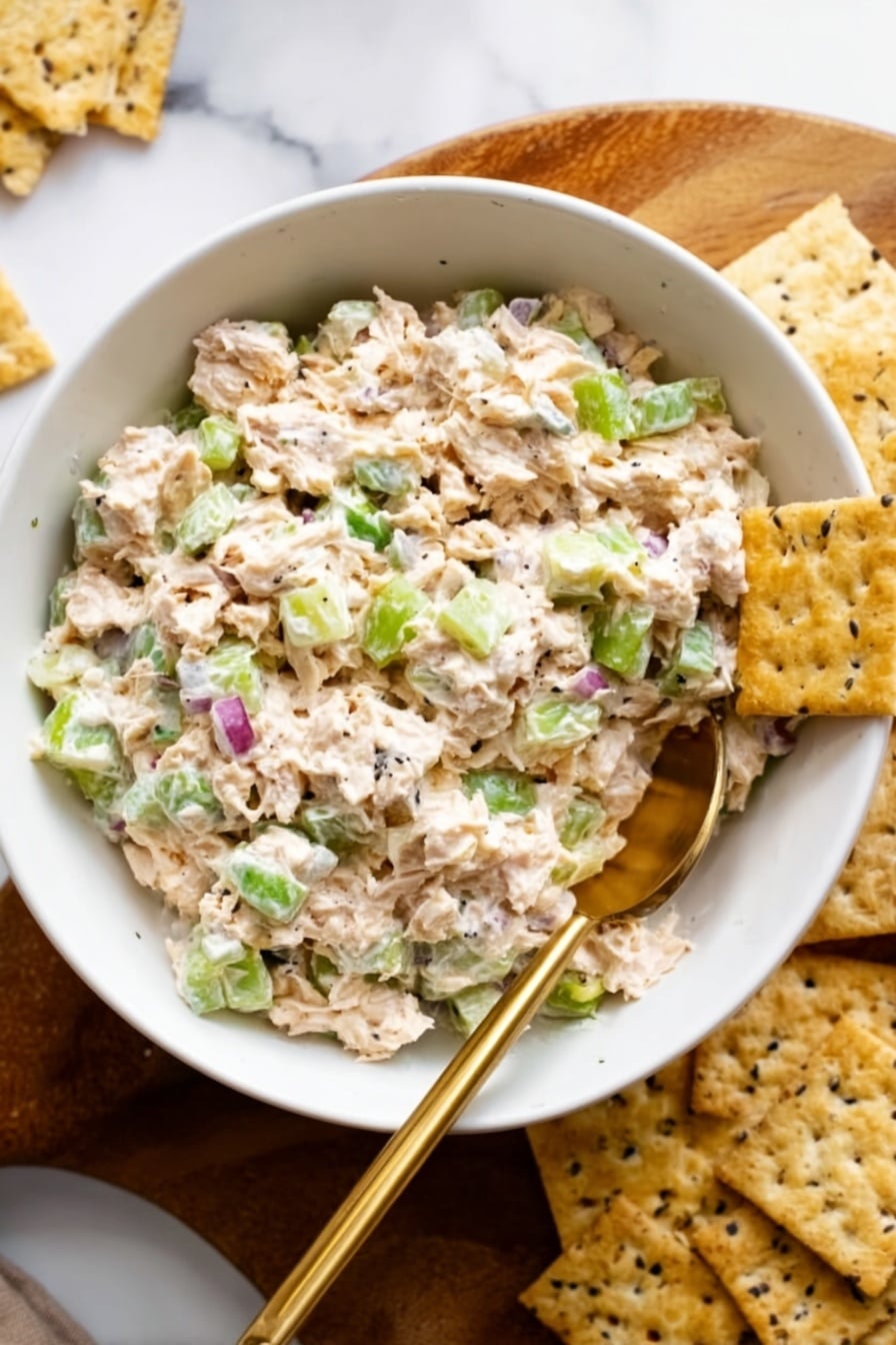 A sandwich with two slices of multigrain bread showing oats and seeds on the crust forms the top and bottom layers. The bottom slice is spread with a green layer that looks like mashed avocado. Above this, there are two bright red tomato slices. On top of the tomato, there is a thick layer of light beige chicken salad mixed with small green and purple bits. The top slice of bread completes the sandwich. It is placed on a white plate with a white marbled surface background. Photo taken with an iphone --ar 2:3 --v 7 - Tunacado Sandwich with Tuna and Avocado, healthy tuna sandwich, avocado tuna salad, quick lunch ideas, nutritious sandwich recipes