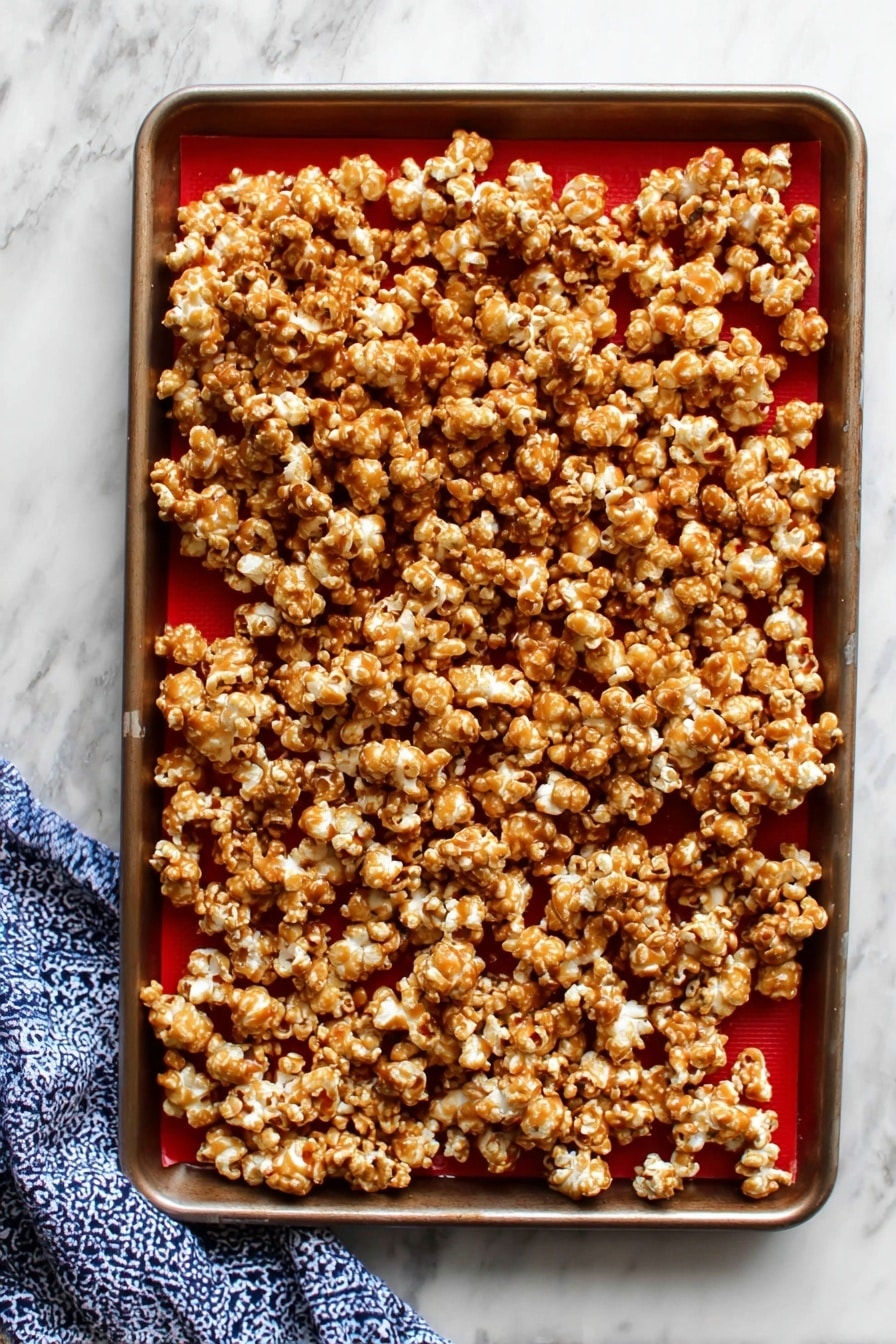 A rectangular white tin box filled with a single thick layer of caramel popcorn, where each popcorn piece is coated unevenly with a shiny golden-brown caramel glaze, showing some light and darker caramel spots. The popcorn looks puffy and slightly sticky, packed tightly inside the box which is lined with white parchment paper that curls over the sides. The box is placed on a surface with a white marbled texture. photo taken with an iphone --ar 2:3 --v 7 - Homemade Caramel Popcorn, caramel popcorn recipe, crispy caramel popcorn, easy caramel popcorn, homemade snack ideas