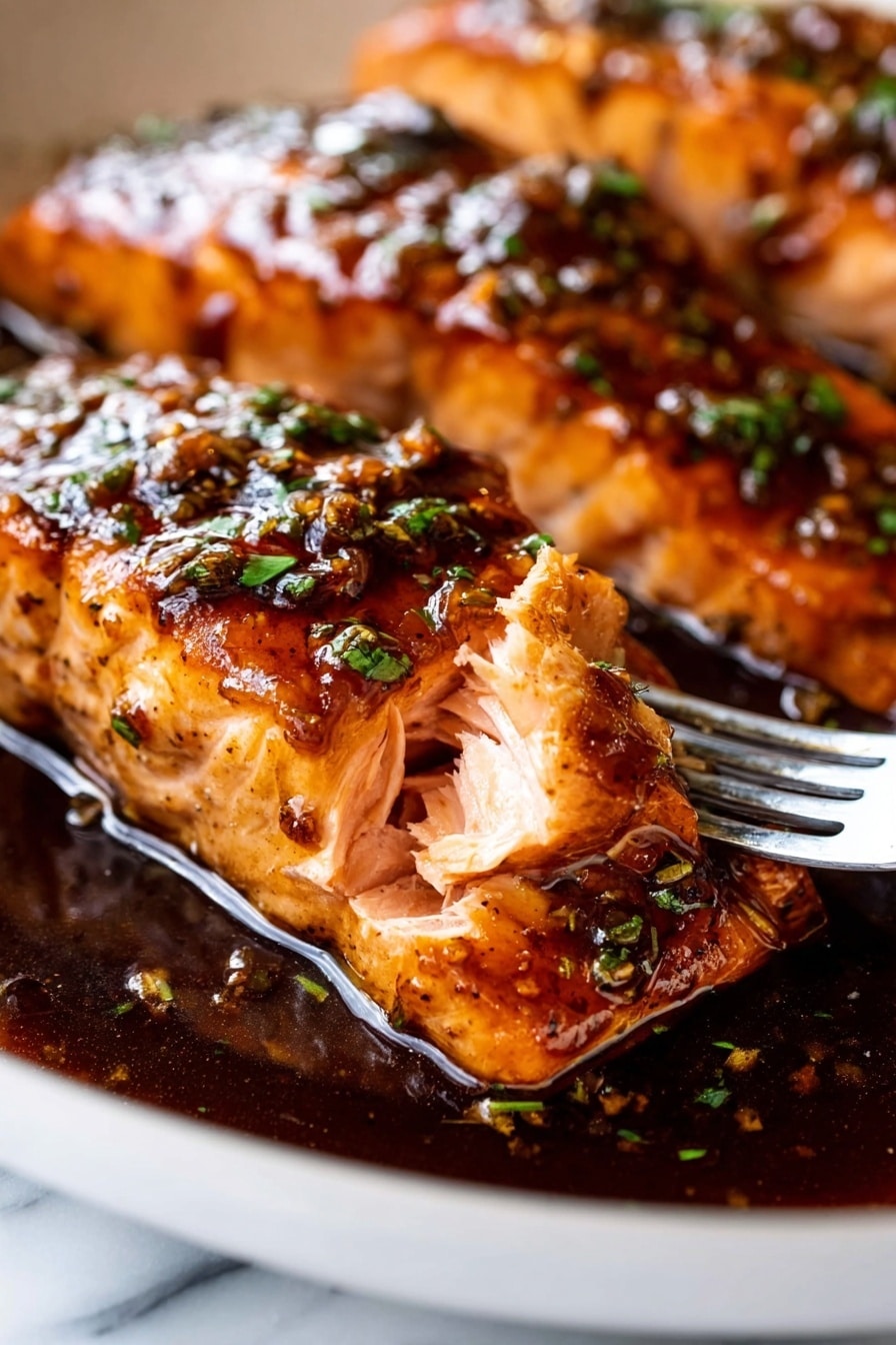 The image shows a close-up of two thick, cooked salmon pieces in a white pan, with the focus on the front piece where a fork pulls a small section showing its light pink, flaky inside layers. The salmon is covered in a shiny, dark brown sauce with a slight glaze and small green herb bits sprinkled on top. The sauce pools around the base of the salmon, reflecting light and adding a rich texture. The pan sits on a white marbled surface, and the salmon skin underneath is visible with a slightly darker color. Photo taken with an iphone --ar 2:3 --v 7 - Honey Garlic Glazed Salmon, Honey Garlic Salmon, Easy Salmon Recipes, Quick Salmon Dinner, Healthy Salmon Recipes
