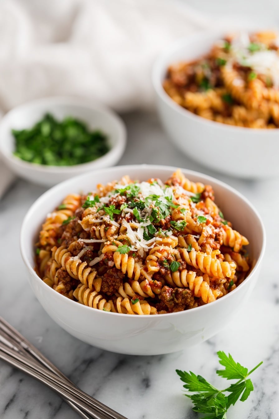 A white bowl filled with a layered pasta dish made of ruffled-edge pasta mixed with a red tomato sauce, ground meat, and small bits of melted cheese, all topped with sprinkles of chopped green parsley. Another similar bowl is in the blurred background beside a small white bowl with more parsley. The bowls are placed on a white marbled surface with a pair of silver chopsticks lying next to the front bowl. Some fresh parsley sprigs are also visible at the bottom right corner. Photo taken with an iphone --ar 2:3 --v 7 - Instant Pot Lazy Lasagna, quick lasagna recipe, easy instant pot dinner, fuss-free lasagna, one-pot lasagna
