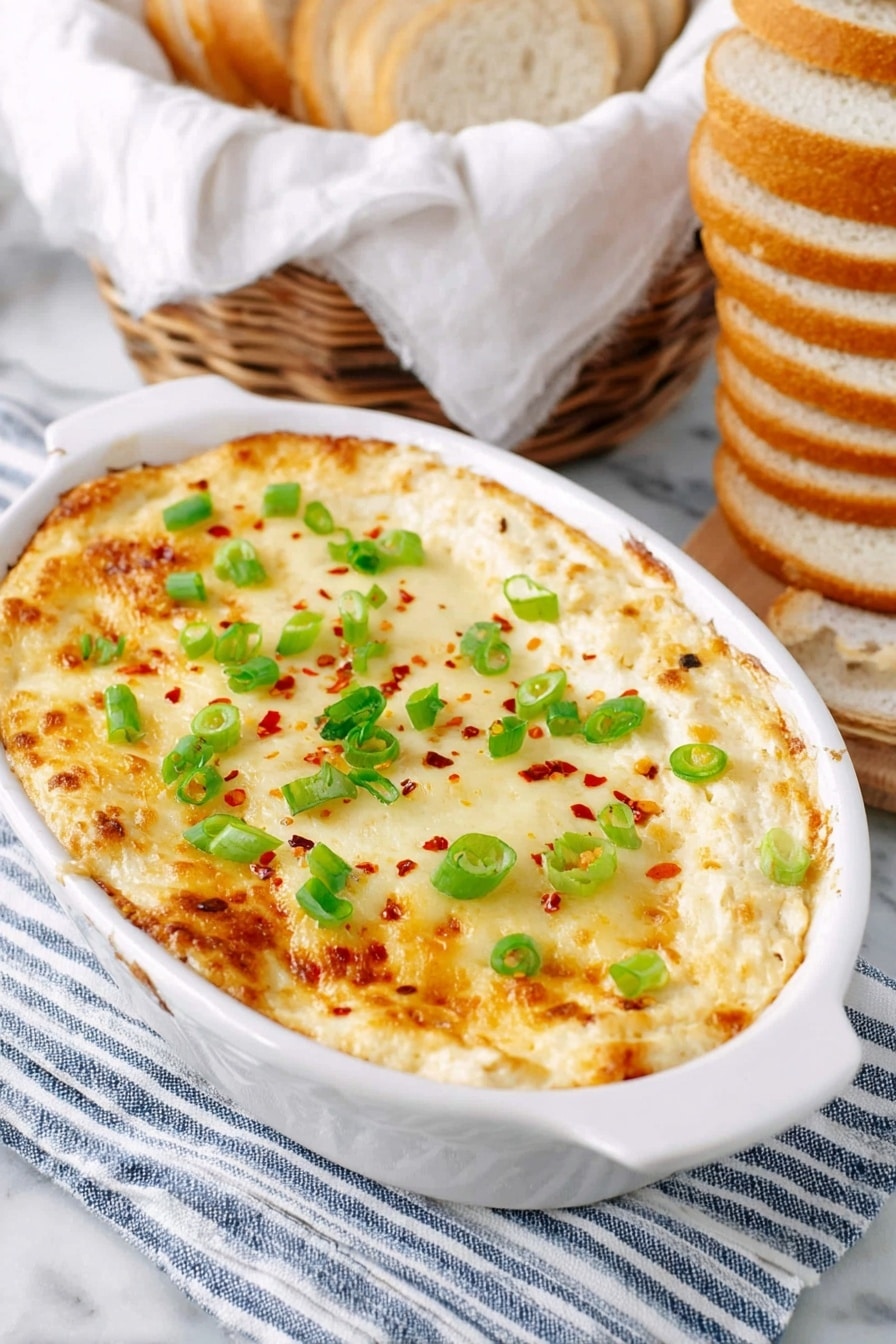 A white oval dish holds a baked dip with a top layer of melted golden cheese, sprinkled with small green spring onion rings and red chili flakes evenly spread. The dish rests on a folded striped blue and white cloth which is on a white marbled surface. To the right of the dish, a stack of sliced round white bread is arranged vertically. In the background, there is a basket with light brown bread lined with a white cloth. Photo taken with an iphone --ar 2:3 --v 7 - Cheesy Roasted Cauliflower Dip, cheesy cauliflower dip, roasted cauliflower appetizer, healthy cauliflower dip, creamy vegetable dip