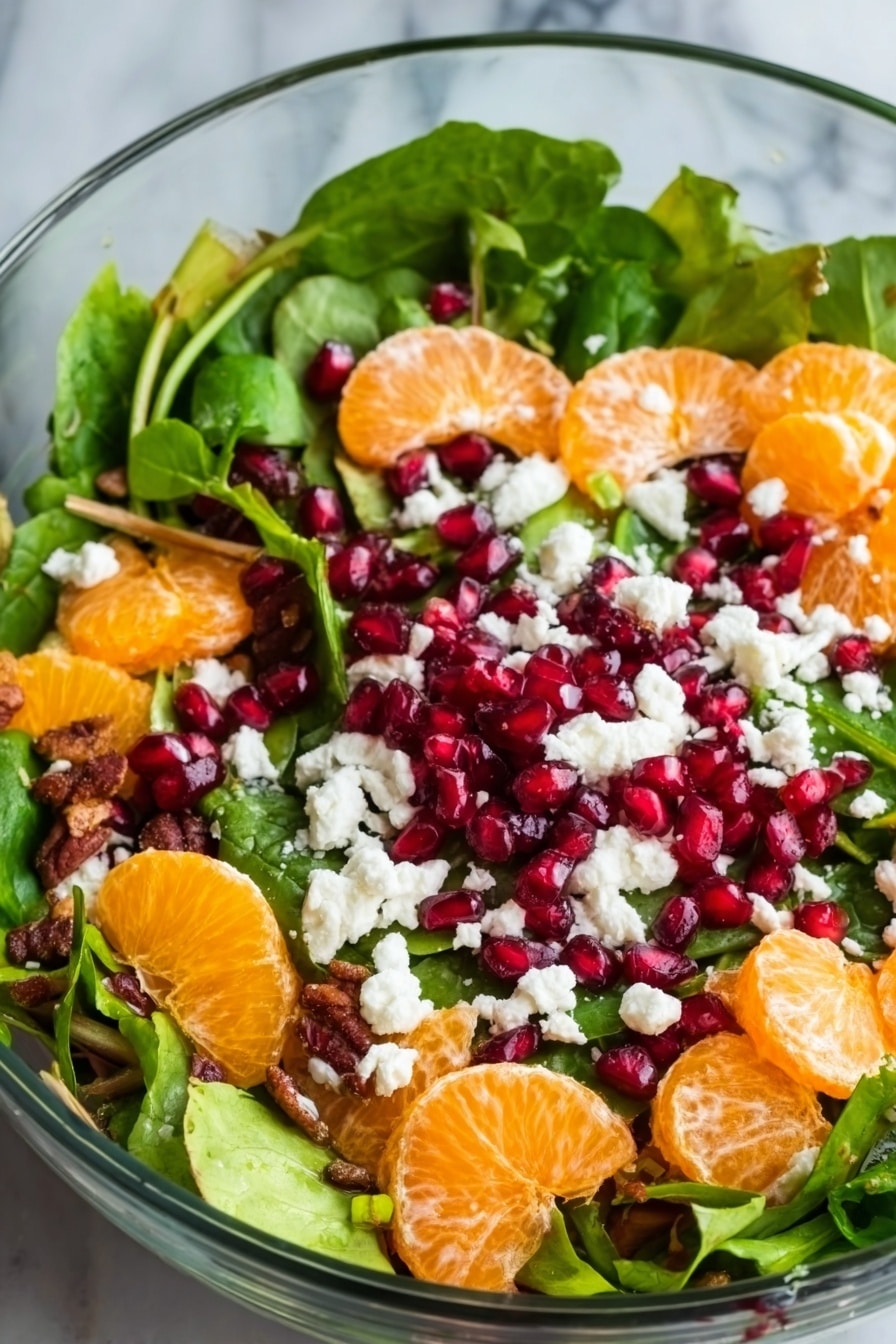 A clear glass bowl holds a fresh salad with three main layers. The bottom layer is a mix of green leafy spinach and lettuce with a soft texture. On top of the greens, there are bright orange mandarin slices spread evenly. Scattered over the salad are small, red pomegranate seeds with a shiny, smooth surface. White crumbled cheese is sprinkled across the top, adding a soft and crumbly texture that contrasts with the fruits and leaves. The background surface is white marble. Photo taken with an iphone --ar 2:3 --v 7 - Festive Citrus Pomegranate Salad, citrus salad with pomegranate, holiday fruit salad, quick holiday salad, healthy festive side dish