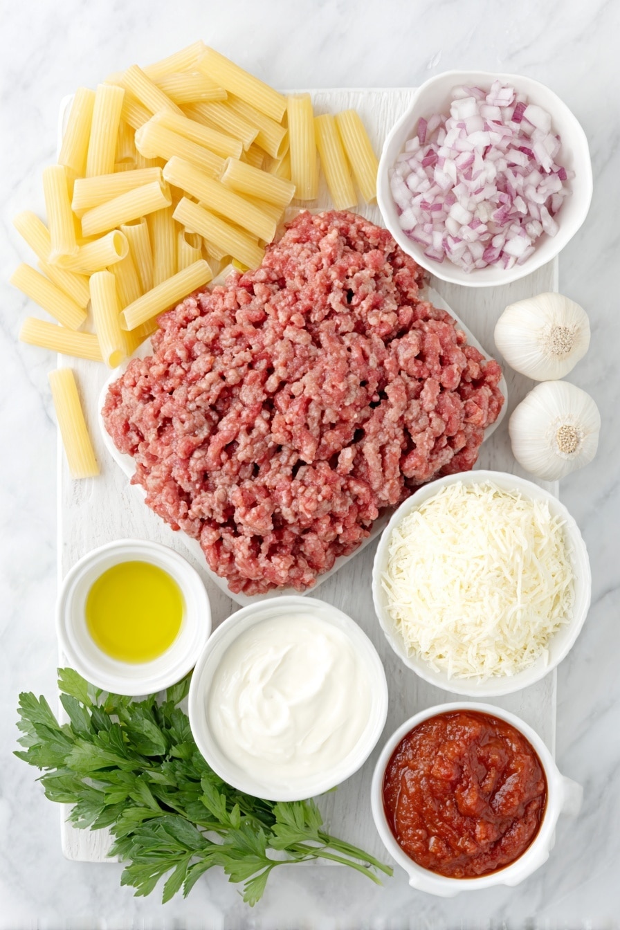 Flat lay of uncooked rigatoni pasta arranged neatly, a small pile of fresh ground Italian sausage with a rich pink-red color, a small white ceramic bowl filled with finely chopped red onion, three whole uncracked garlic cloves with smooth white skins, a small white ceramic bowl containing vibrant red tomato paste, a small white ceramic bowl of thick heavy cream, a small white ceramic bowl heaped with grated Parmesan cheese, a tiny white ceramic bowl holding bright red-orange red pepper flakes, a small white ceramic bowl with coarse salt crystals, a small pat of golden butter, a small white ceramic bowl of glossy olive oil, and a small bunch of fresh flat-leaf parsley with bright green leaves, all arranged with perfect symmetry and balanced proportions, placed on a clean white marble surface, soft natural light, photo taken with an iPhone, professional food photography style, fresh ingredients, white ceramic bowls, no bottles, no duplicates, no utensils, no packaging --ar 2:3 --v 7 --p m7354615311229779997 - Spicy Sausage Rigatoni Pasta, spicy sausage pasta, creamy rigatoni recipe, quick pasta dinner, easy Italian sausage pasta