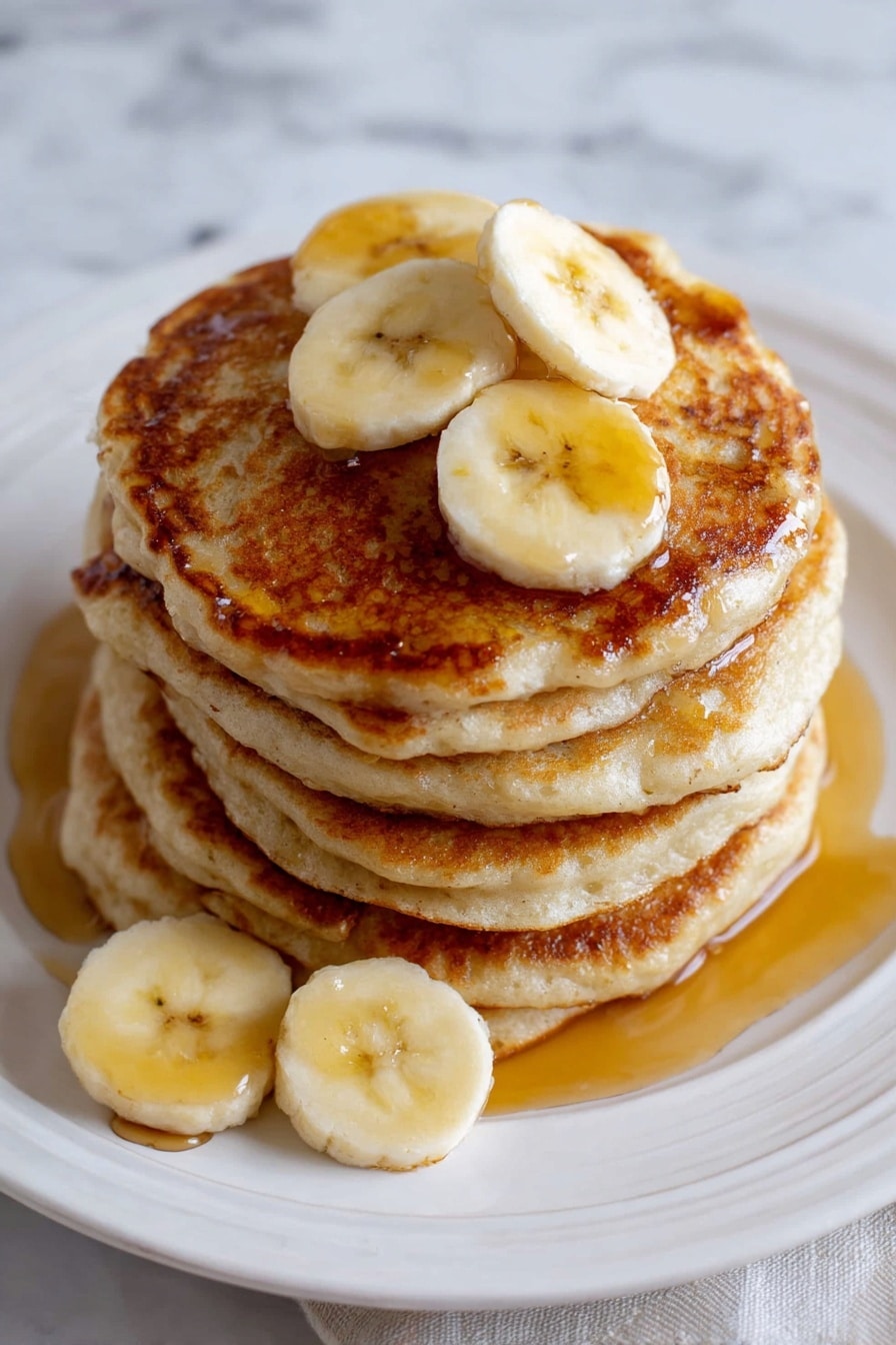 A stack of six thick, golden-brown pancakes sits in the center of a white plate with a slightly embossed edge. The top pancake is topped with three slices of yellow banana, and syrup is drizzled over the pancakes, pooling slightly on the plate and wrapping around the sides. Two more banana slices rest on the plate near the front of the stack. The white plate is set on a surface with a white marbled texture. Photo taken with an iphone --ar 2:3 --v 7 - Banana Pancakes, easy banana pancakes, fluffy banana pancakes, breakfast banana pancakes, healthy banana pancakes