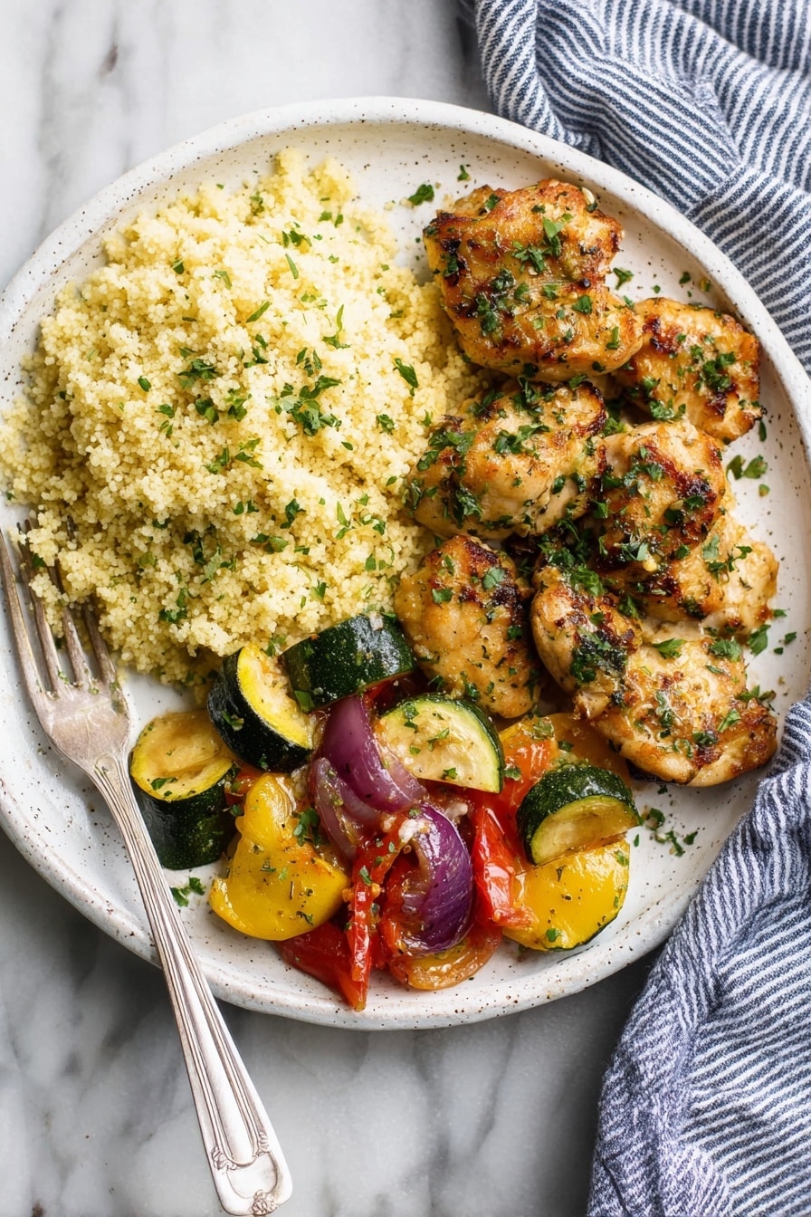 A white speckled plate holds a meal with three sections: on the left, a fluffy mound of light yellow couscous with small green herb sprinkles; in the center and right, several pieces of golden brown chicken with a slightly crispy texture, coated in green chopped herbs; at the bottom, a mix of cooked vegetables including glossy yellow squash, green zucchini slices, red tomato chunks, and purple onion wedges, all with a slight char. A silver fork rests on the left side of the plate, placed on a white marbled surface. A blue and white striped cloth is visible on the right side of the image. Photo taken with an iphone --ar 2:3 --v 7 - Garlic Butter Chicken Bites, chicken bites with garlic butter, quick chicken dinner ideas, easy chicken recipes, flavorful chicken recipes