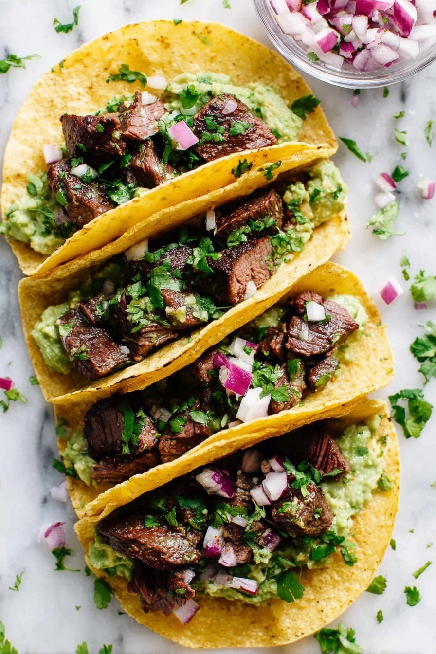 Four yellow corn tortillas are filled and folded in half, each stacked with three layers: a creamy green guacamole base, topped with chunky dark brown pieces of grilled steak, and garnished with small, diced purple and white onions along with fresh green cilantro leaves sprinkled over all. The tacos are placed closely on a white marbled surface, with some onion pieces and cilantro leaves scattered around. A clear glass bowl with diced red onions is partially visible in the upper right corner. The photo taken with an iphone --ar 2:3 --v 7 - Marinated Mojo Steak Tacos, mojo steak tacos, quick guacamole recipe, citrus steak tacos, flavorful taco recipes