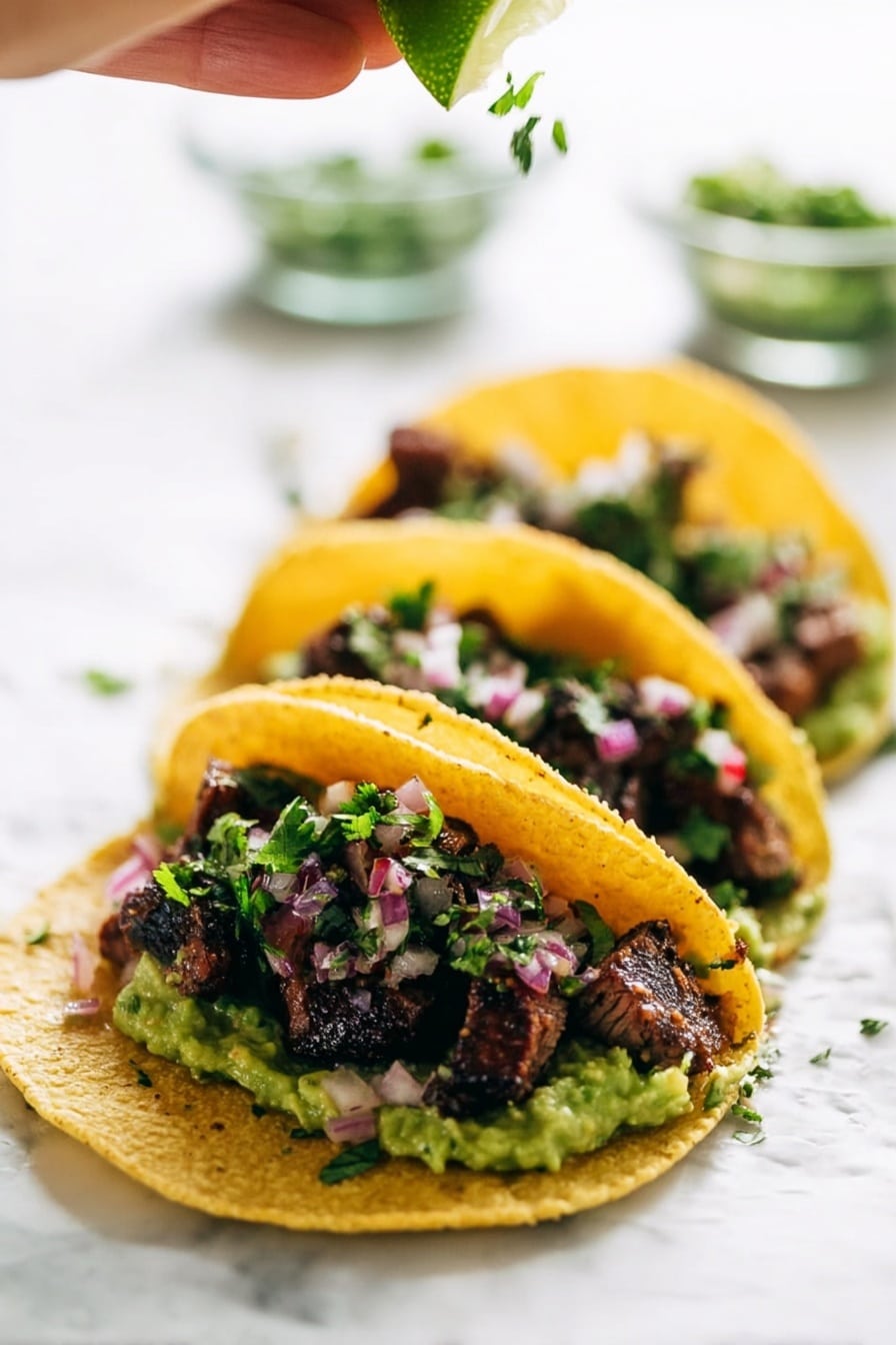Three tacos are lined up on a white marbled surface, each taco made with a yellow corn tortilla that holds several layers. The bottom layer is chunky green guacamole, topped with small pieces of grilled dark brown meat with a slightly charred texture. Sprinkled over the meat are small bits of fresh green cilantro and finely chopped pinkish-red onions. Above the tacos, a woman's hand is squeezing a fresh lime wedge, adding a bright green color and a juicy texture to the scene. The background is softly blurred with clear glass bowls holding more chopped herbs and onions. Photo taken with an iphone --ar 2:3 --v 7 - Marinated Mojo Steak Tacos, mojo steak tacos, quick guacamole recipe, citrus steak tacos, flavorful taco recipes