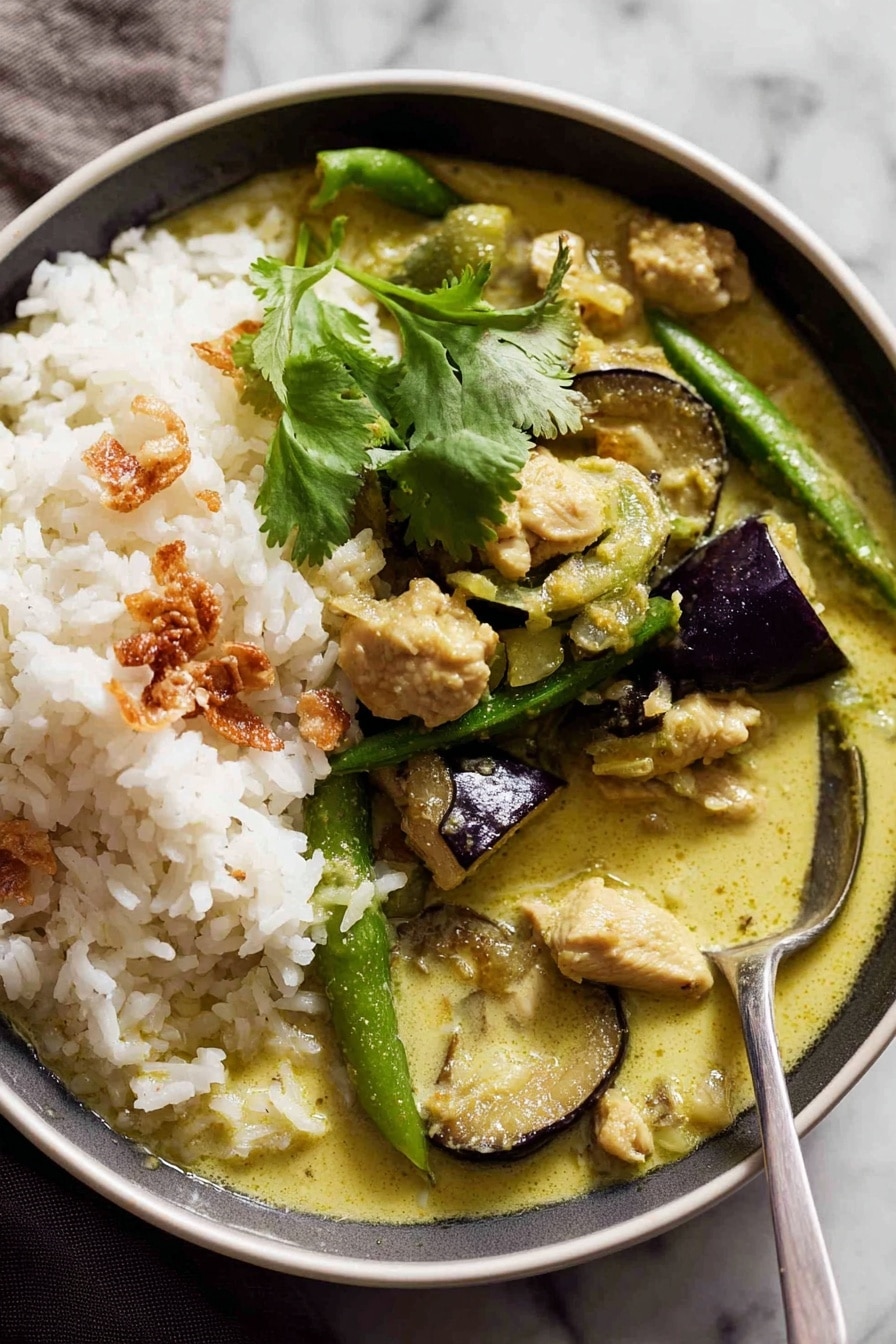 A white bowl filled with two main layers: on one side, a mound of plain white rice with a sprig of fresh green cilantro on top, and on the other side, creamy green curry sauce with pieces of soft green eggplant slices, light green sugar snap peas, tender chunks of chicken, and some golden crispy fried shallots scattered on top. A silver spoon rests inside the curry, partly lifting some rice and sauce. The bowl sits on a white marbled surface, and there is a soft brown cloth partly visible in the background. Photo taken with an iphone --ar 2:3 --v 7 - Easy Thai Green Curry with Chicken, Thai green curry recipe, quick chicken curry Thai, authentic Thai green curry, spicy green curry with chicken