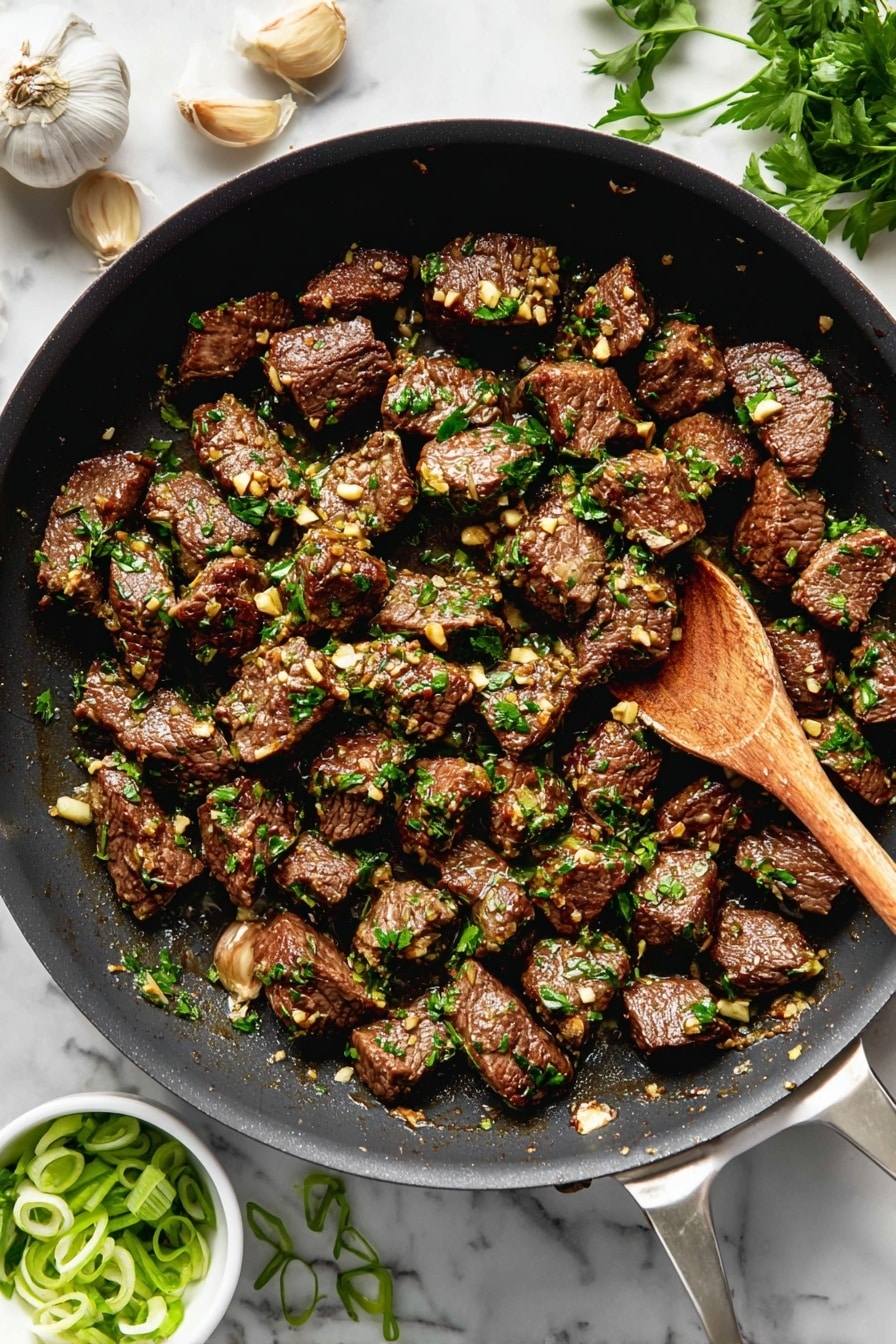 The image shows a black frying pan filled with many evenly sized pieces of cooked beef, browned on the outside. Each piece is covered with small bits of garlic and sprinkled with fresh green herbs, mostly chopped parsley. In the pan is a wooden spoon stirring the beef. Around the pan on a white marbled surface are garlic cloves, some green herbs, and a small white bowl with sliced green onions. The colors in the dish include dark brown from the beef, light golden from the garlic, and bright green from the herbs. Photo taken with an iphone --ar 2:3 --v 7 - Garlic Butter Steak Bites, Garlic Butter Steak Bites recipe, easy steak bites, flavorful steak appetizer, quick weeknight steak