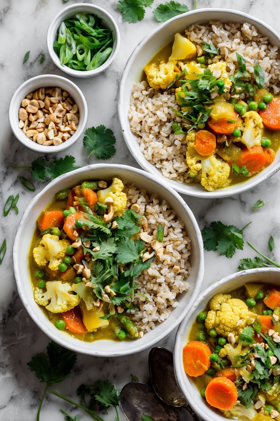The image shows three white bowls filled with a colorful vegetable curry and brown rice. Each bowl has two main sections: one side has light brown, fluffy rice, and the other side is filled with a mix of vegetables like orange carrots, green peas, and yellow cauliflower, all coated in a creamy yellow curry sauce. Fresh green cilantro leaves and sliced green onions are sprinkled on top, adding a fresh touch. Around the bowls, small white ramekins hold chopped nuts and extra green onions. The bowls and ramekins are placed on a white marbled surface with scattered cilantro leaves, and an old silver spoon rests nearby. Photo taken with an iphone --ar 2:3 --v 7 - Thai Peanut Coconut Cauliflower Curry, Thai cauliflower curry, vegan cauliflower curry, coconut cauliflower stir-fry, quick plant-based Thai curry